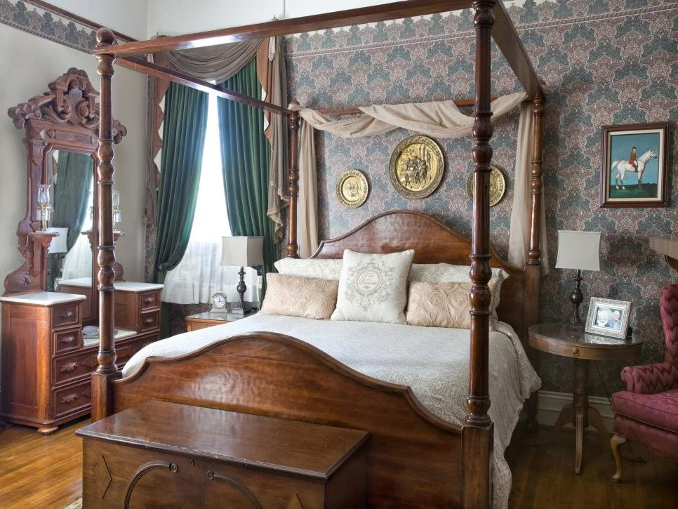Vintage bedroom with a four-poster bed, ornate wood furniture, floral wallpaper, and antique decor.