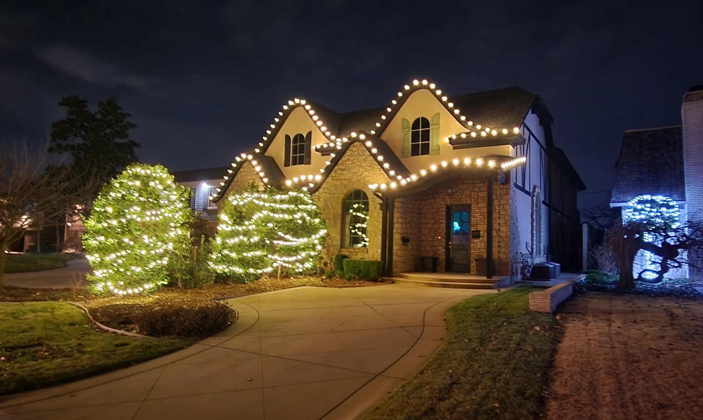 House decorated with Christmas lights at night, with lit windows and illuminated trees in the yard.