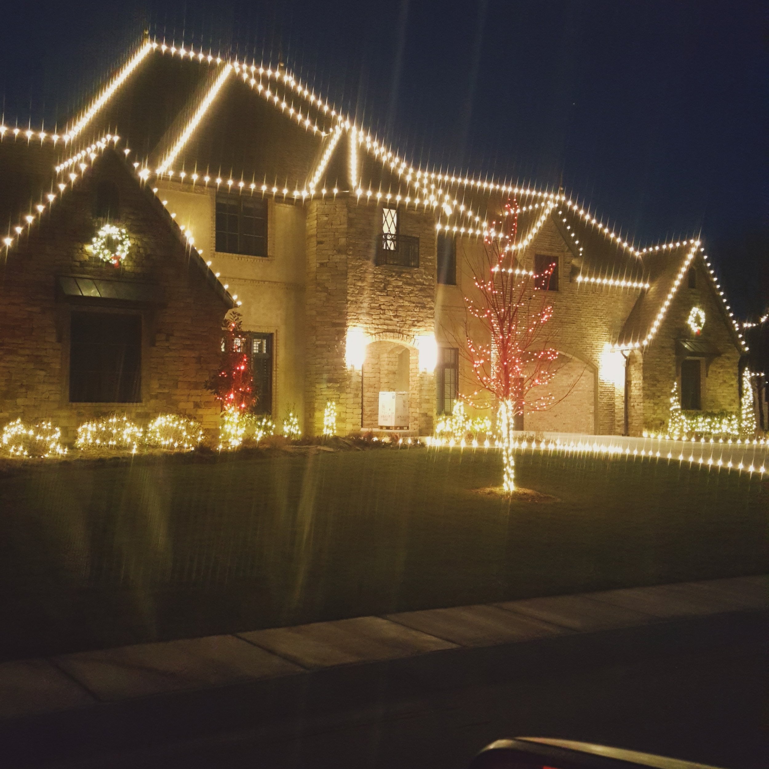 A large house decorated with Christmas lights, wreaths, and illuminated trees at night.