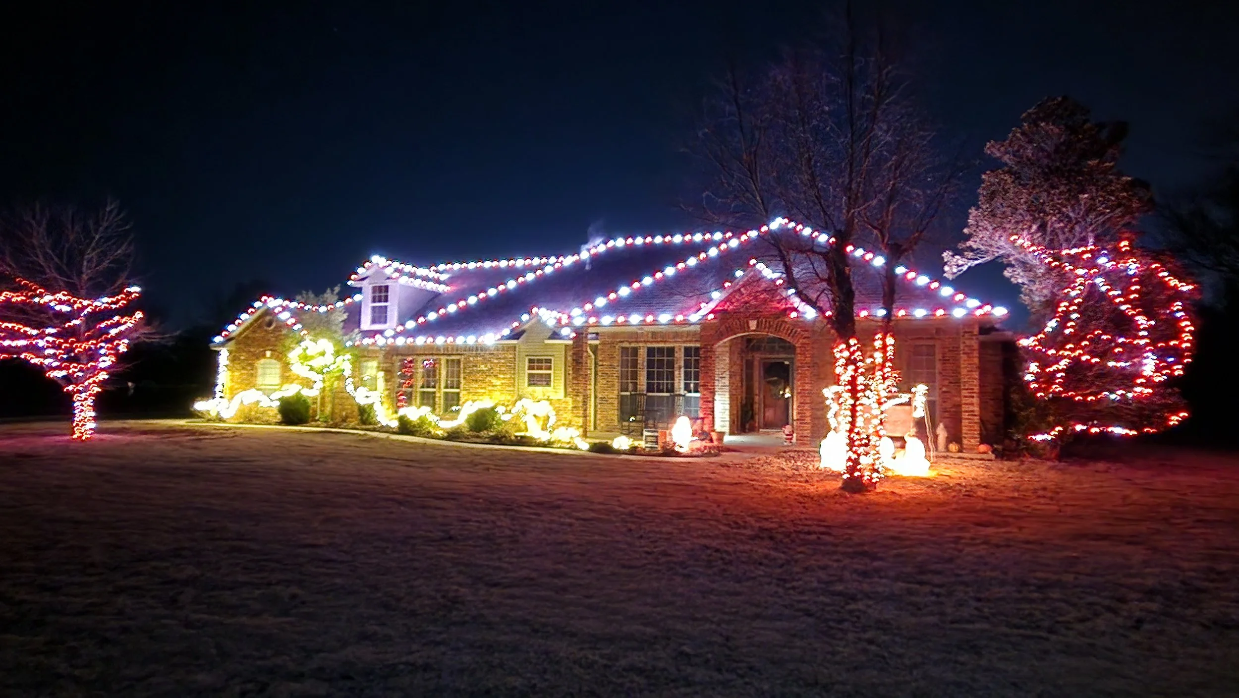 House decorated with Christmas lights at night, with illuminated trees and holiday decorations.