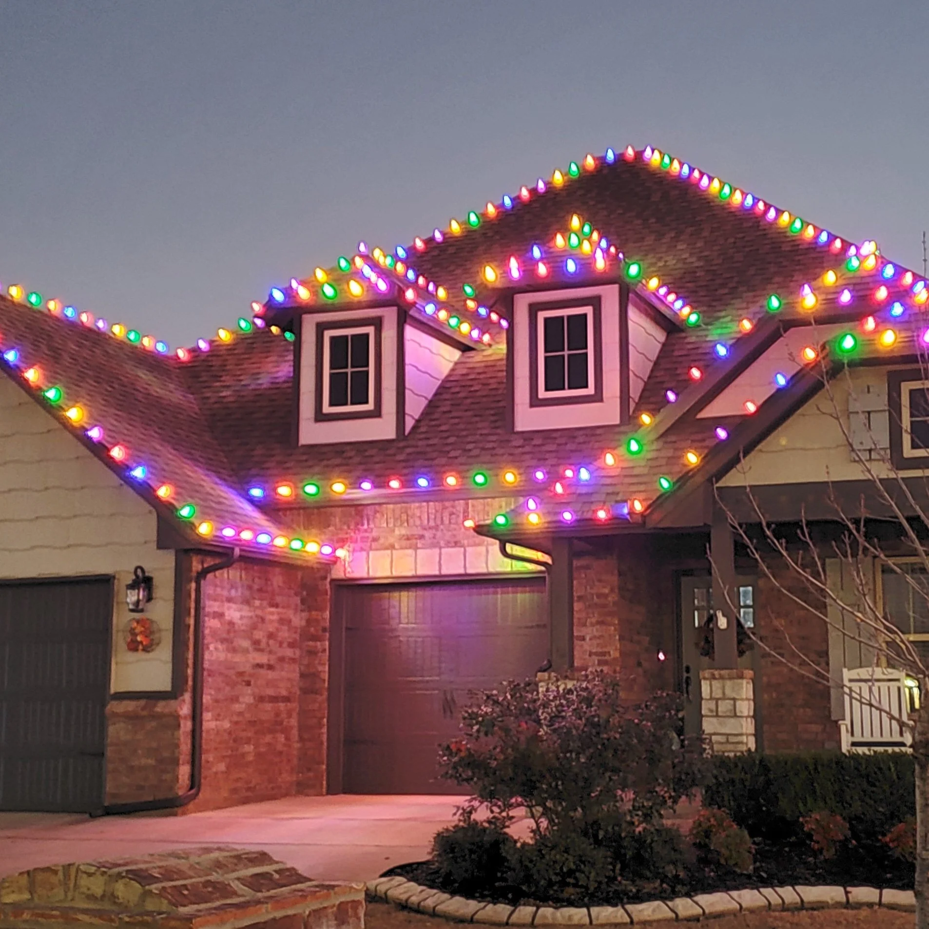A house decorated with colorful Christmas lights outlining the roof edges and dormer windows.