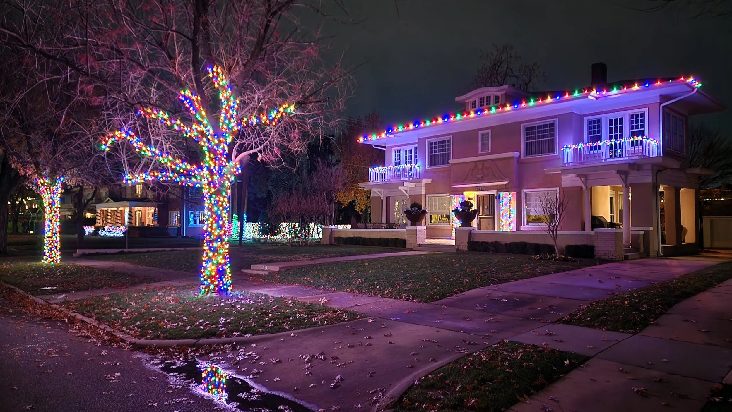 House decorated with colorful Christmas lights at night, with lit trees and decorated walkways.