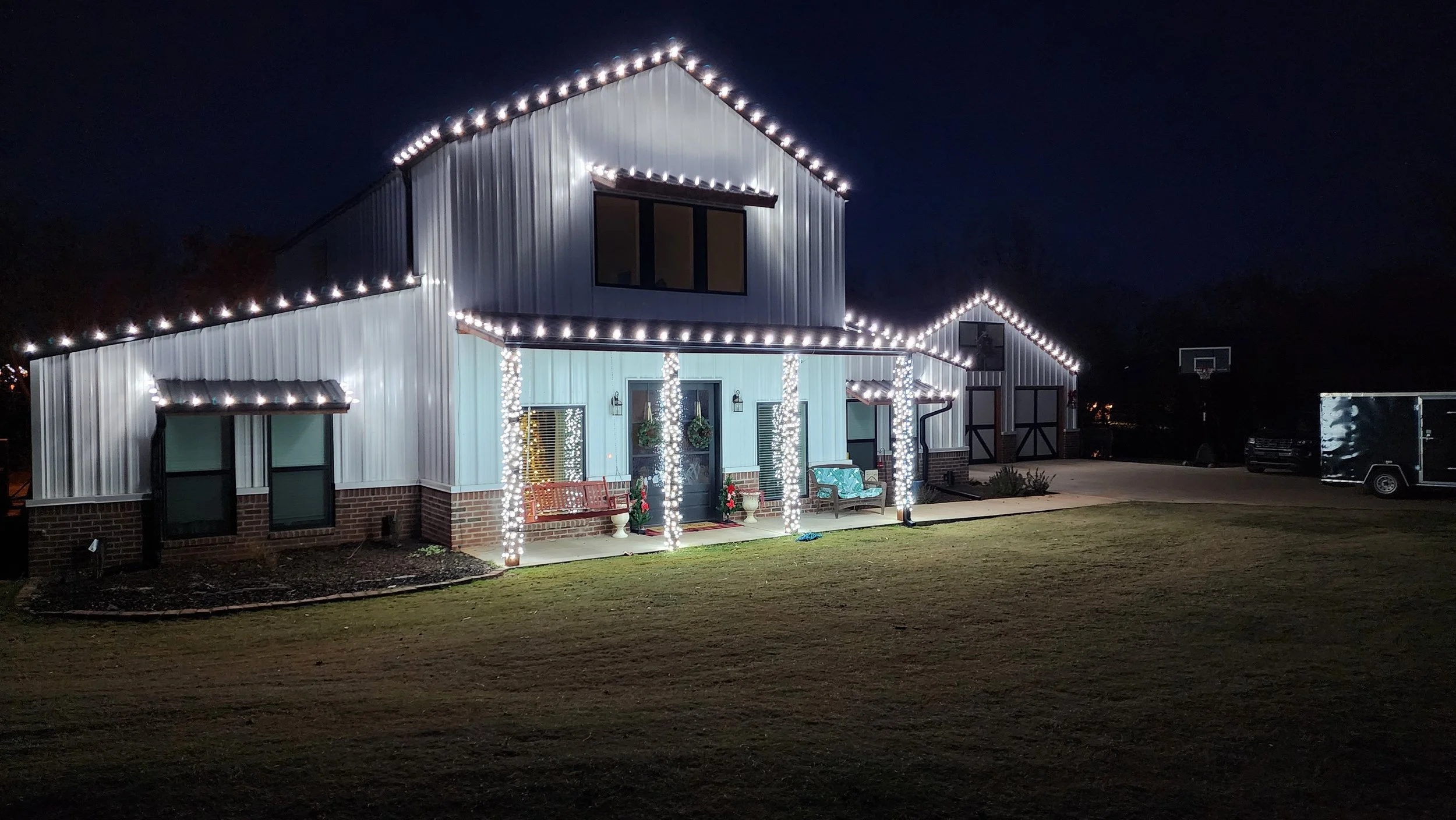 A house decorated with white string lights outlining the roof and pillars on the porch at night.