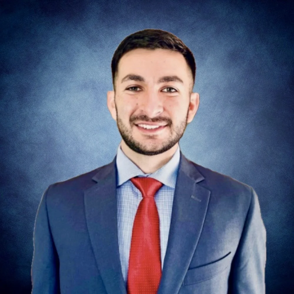 Businessman in a suit with a red tie smiling in front of a blue background.