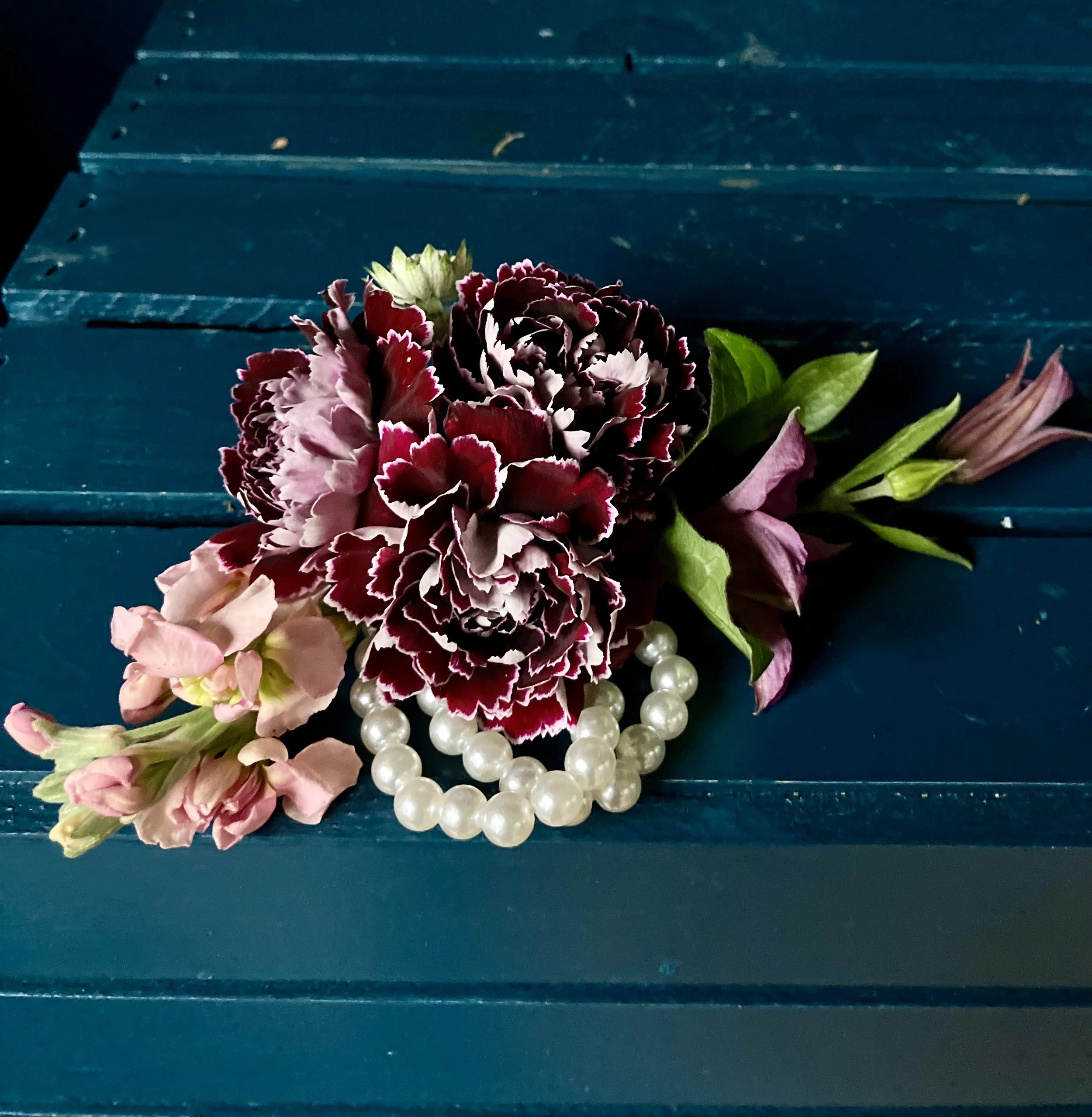 Fresh wrist prom corsage with carnations and clematis displayed in Portland florist studio