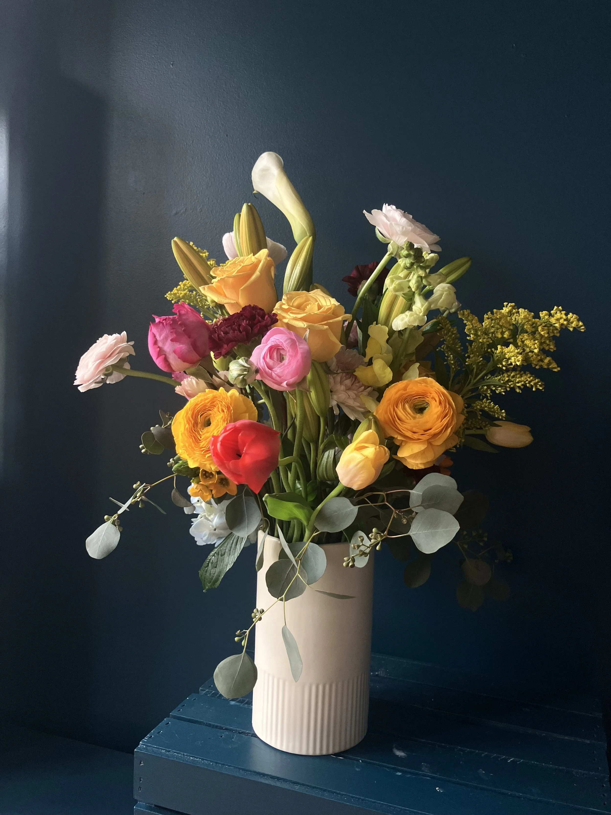 Dense seasonal flower arrangement for spring with focal blooms of multi-hued ranunculus, tulips, lilies and foliage