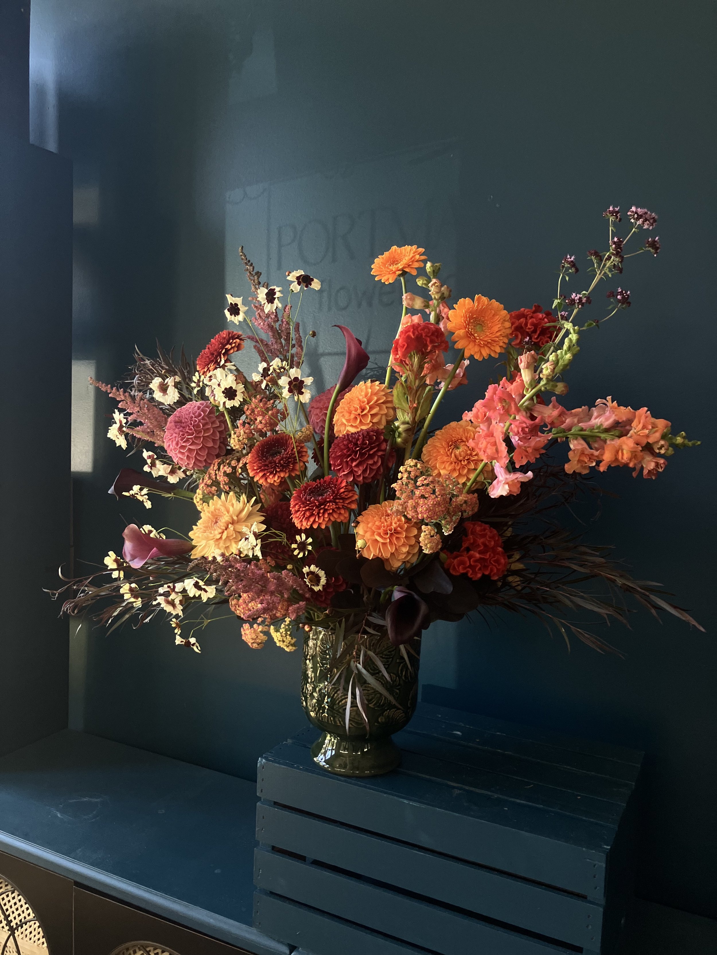 Large arrangement in a vase against dark background, with sunset colored blooms designed in season by Portmanteau in Portland
