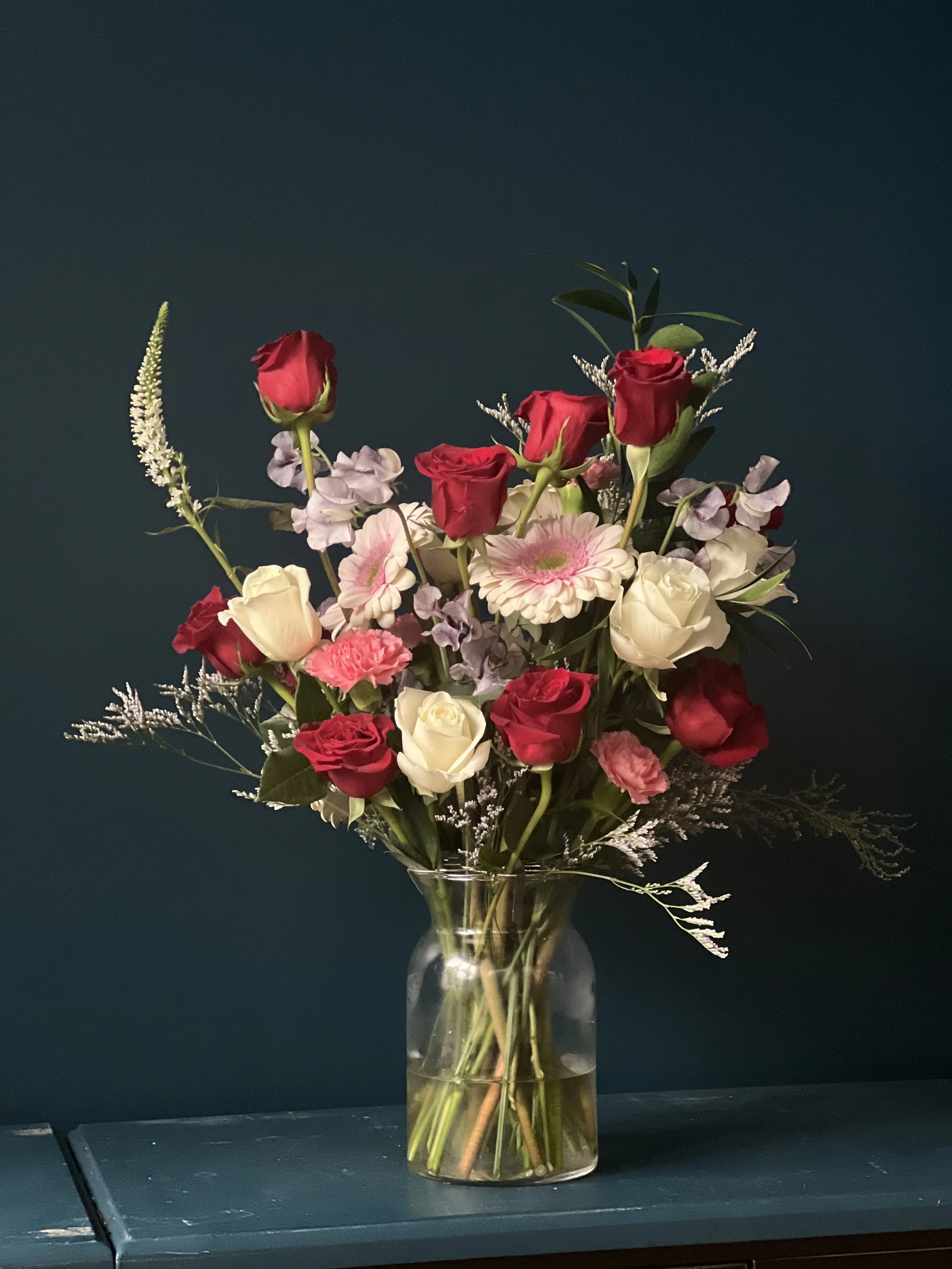 Sculptural Valentine’s Day flower arrangement with red roses, soft pink and white blooms, airy white foliage, and sweet pea accents in a glass vase, for Portland, Oregon delivery.