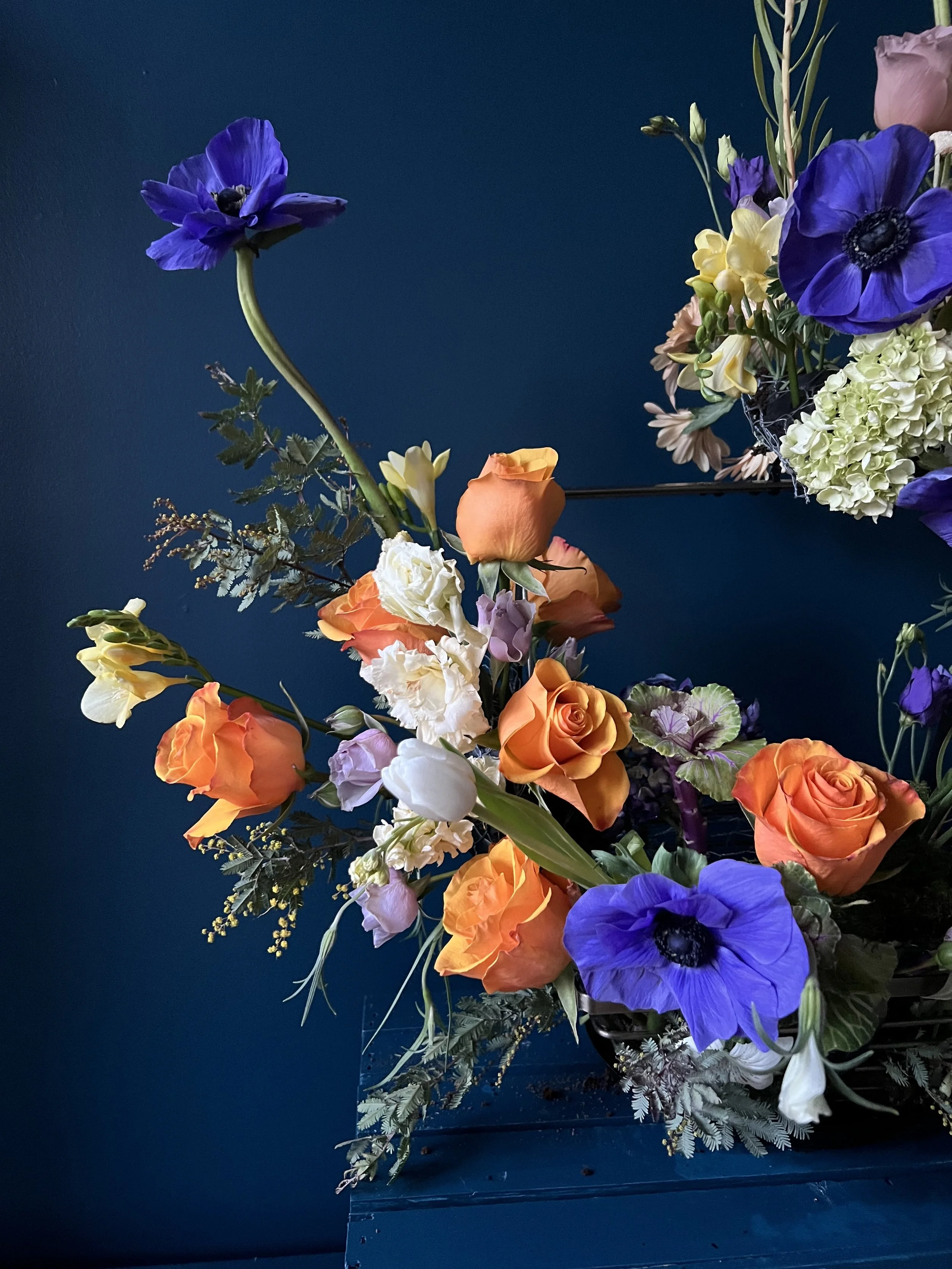 A close view of part of a floral centerpiece showing light hydrangea, orange roses, freesia and deep blue anemones