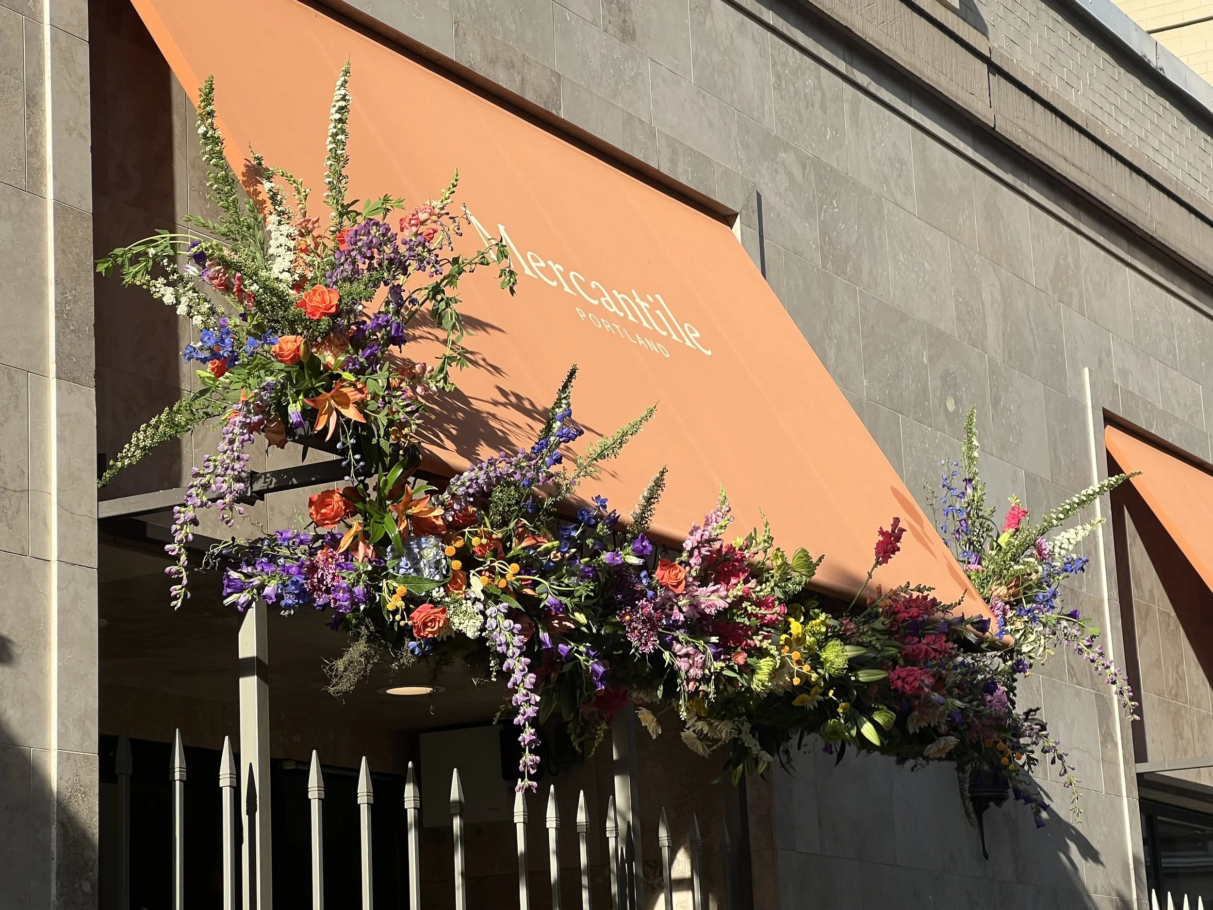 A hanging installation of vibrant flowers for a Portland business event and their storefront awning
