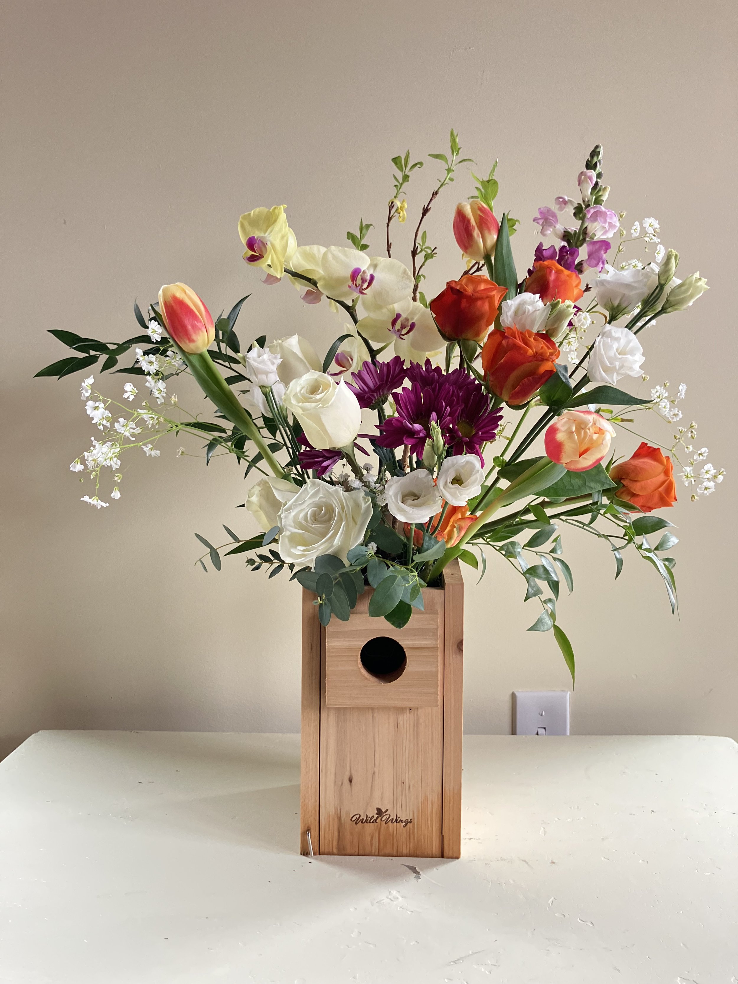 White & orange roses, tulips, purple pea and an orchid perched in a box