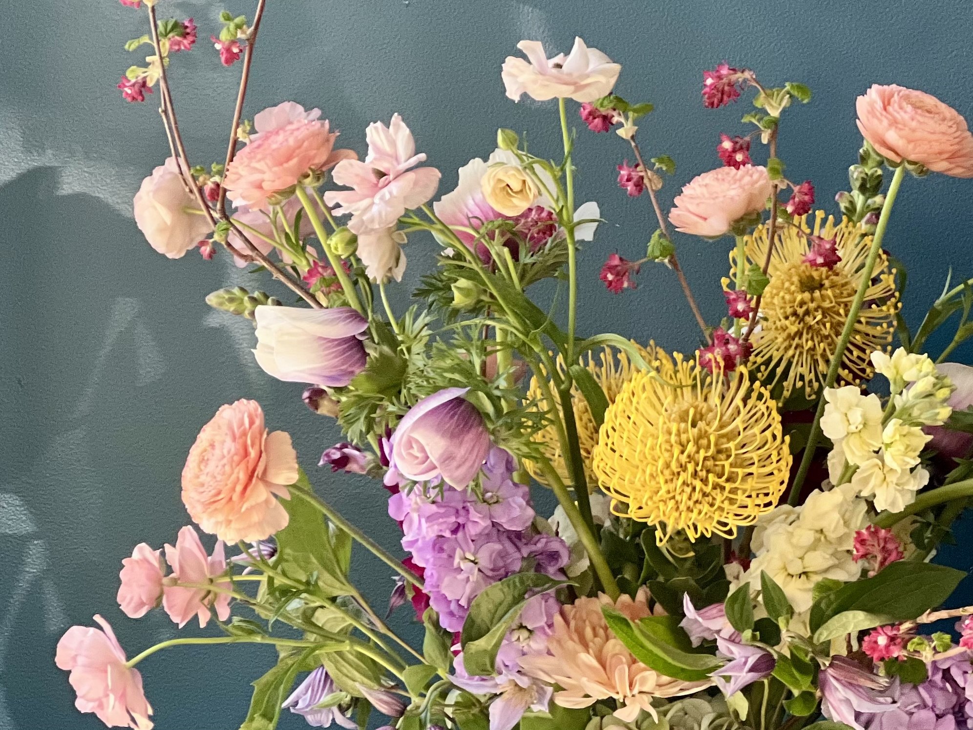 Close-up of yellow protea, anemone, and ranunculus in airy sculptural spring floral arrangement with rich color contrast