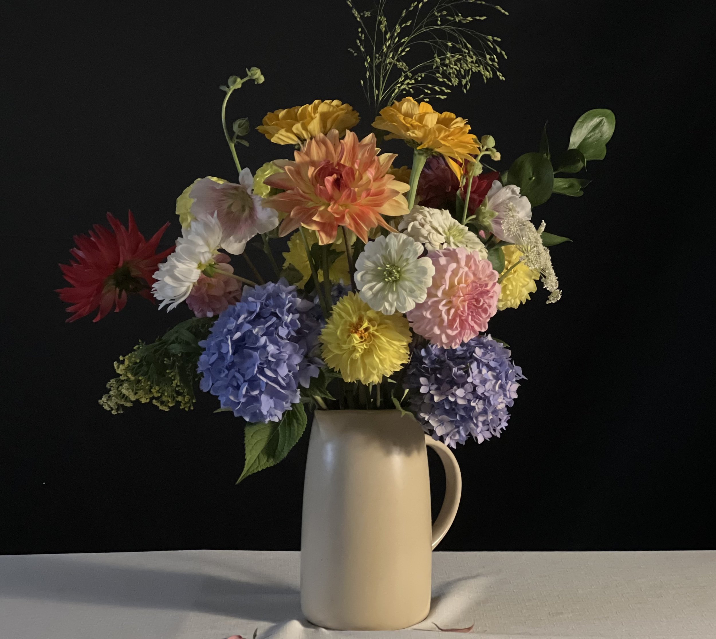 An impressive, inventive display of blue hydrangeas, zinnias & dahlias contrasting on a table vessel