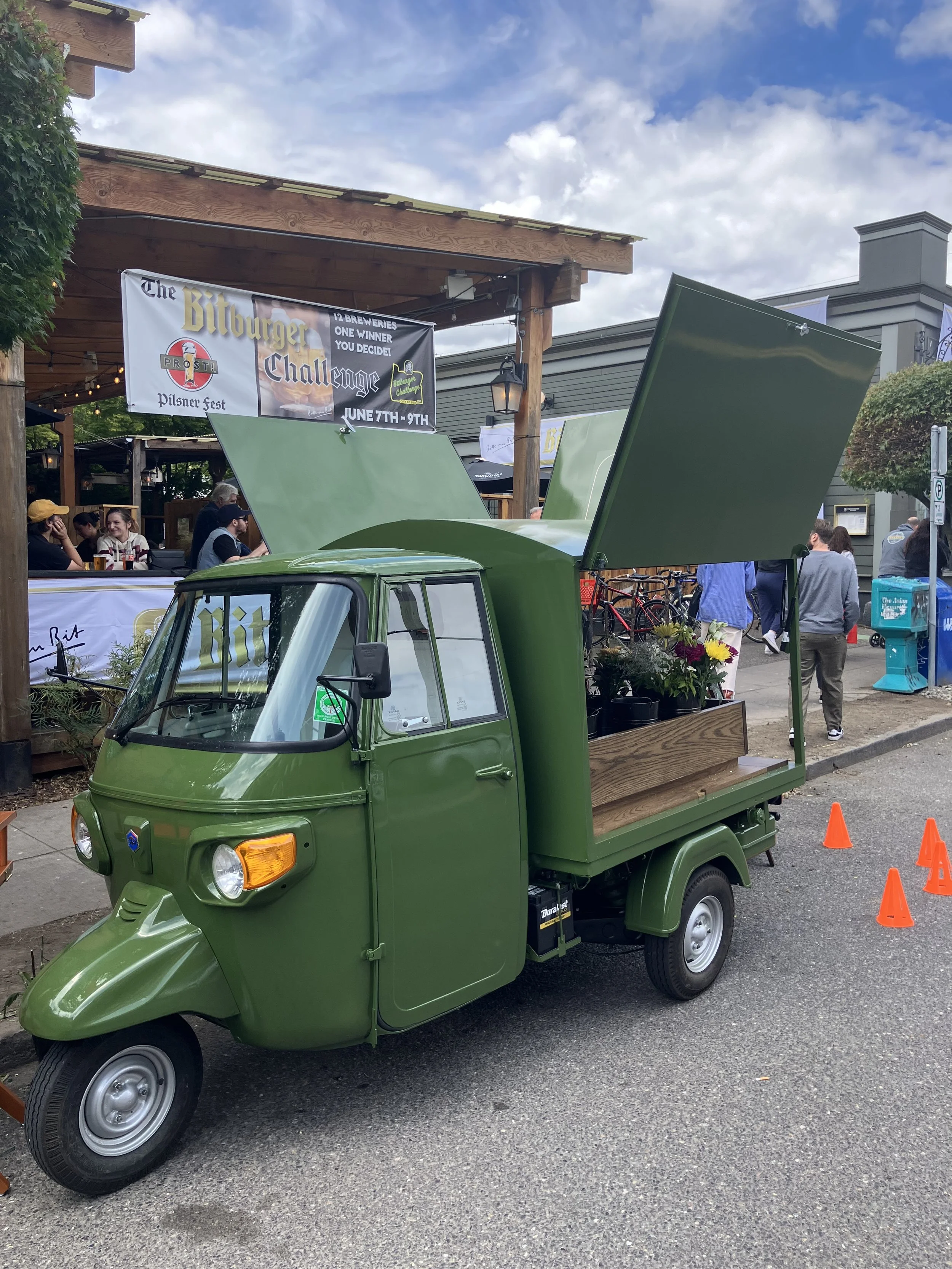 A mobile pop-up floral vendor in green truck outside a busy food court