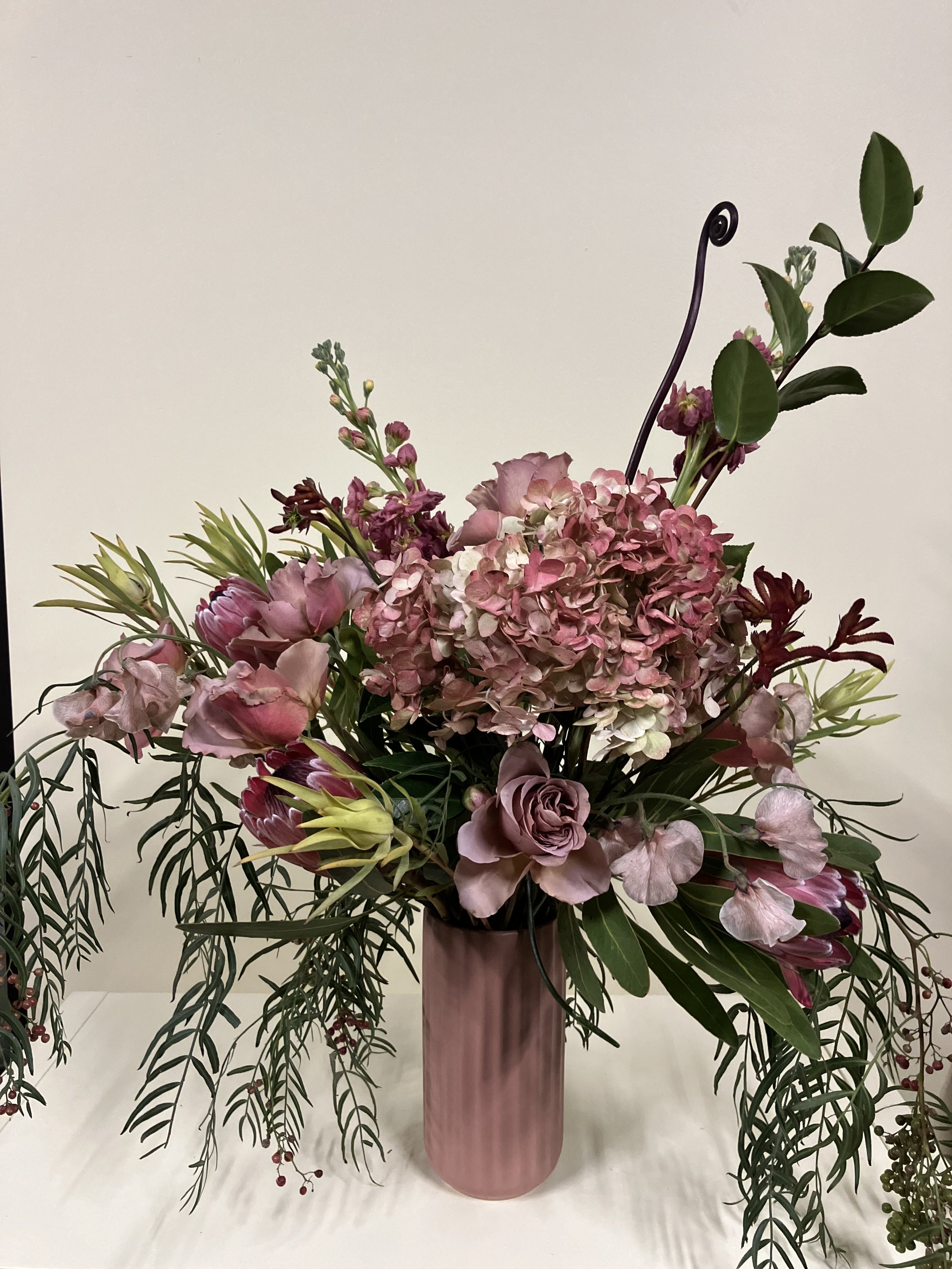 large display of blooms in shades of red and pink with profuse foliage arranged in a vase