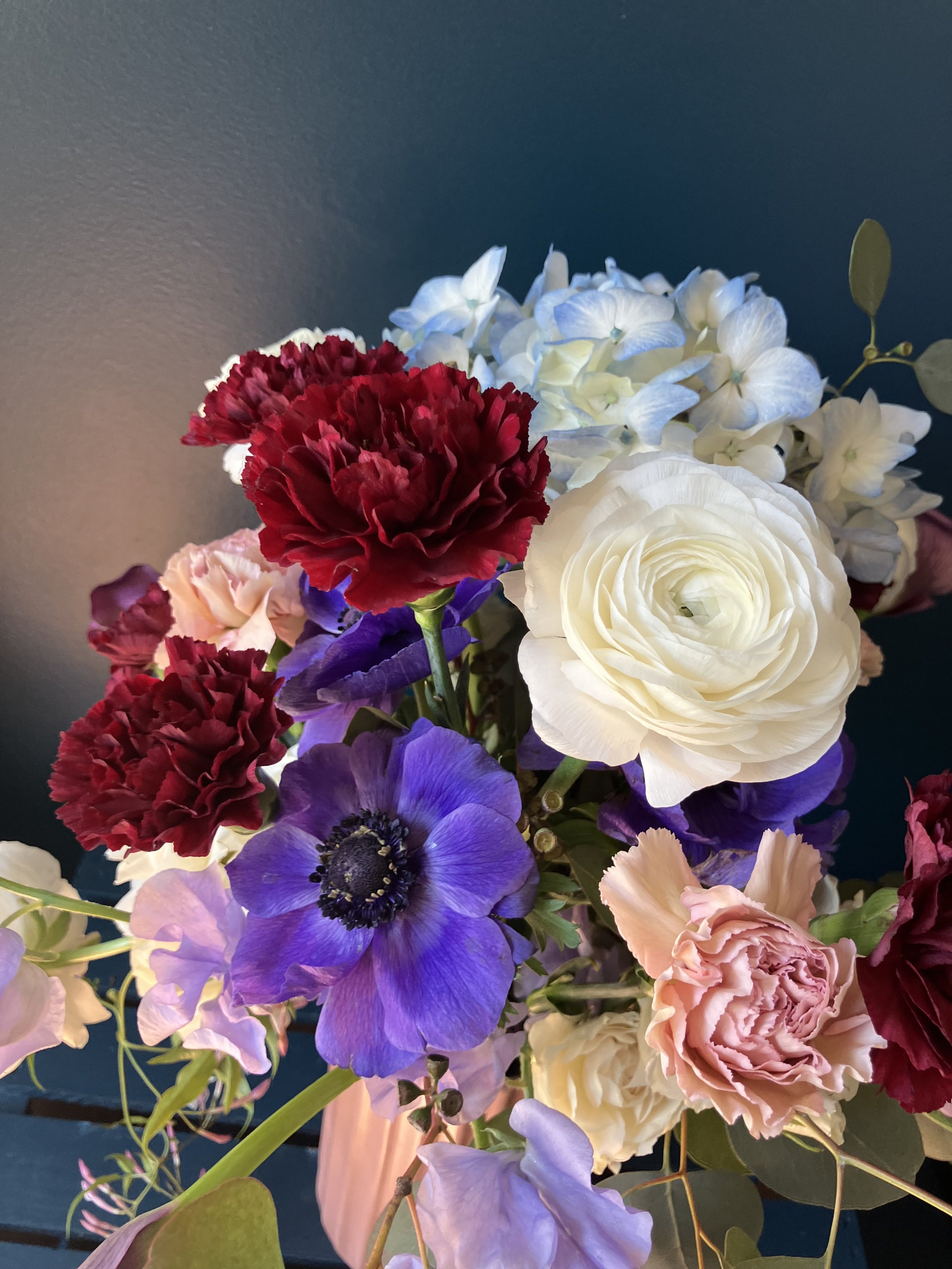 Intricate and swirling sight of the flower-heads of red & antique carnation, blue hydrangea, purple anemone & white ranunculus