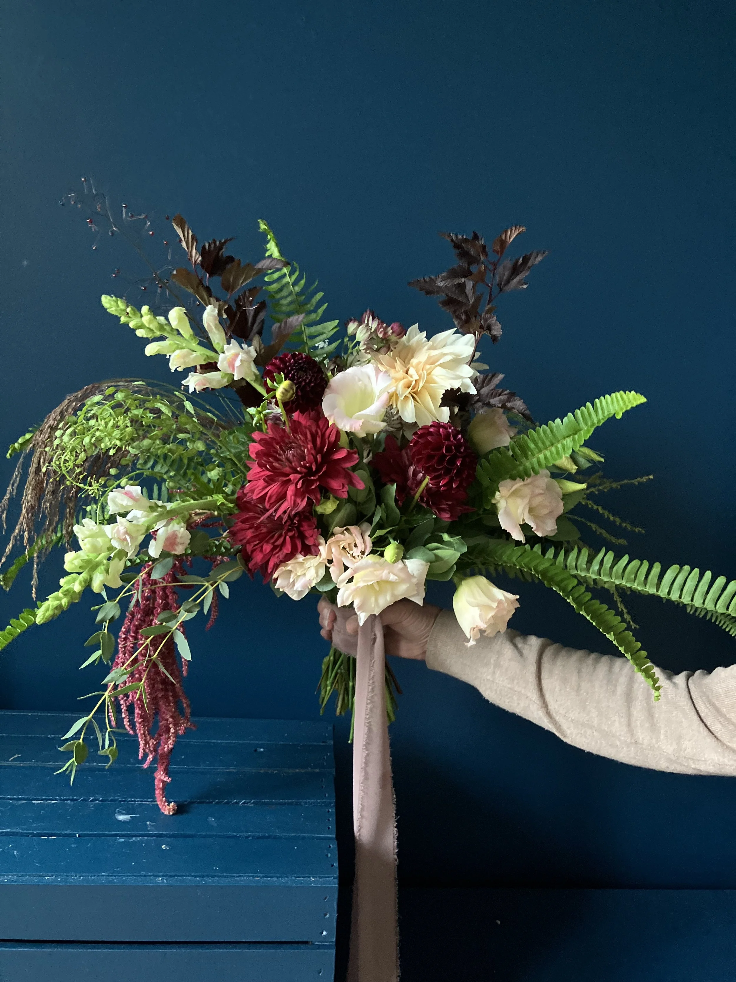 Designer holding a bridal bouquet made for a Portland wedding, ribboned and featuring lisianthus, mums and ferns