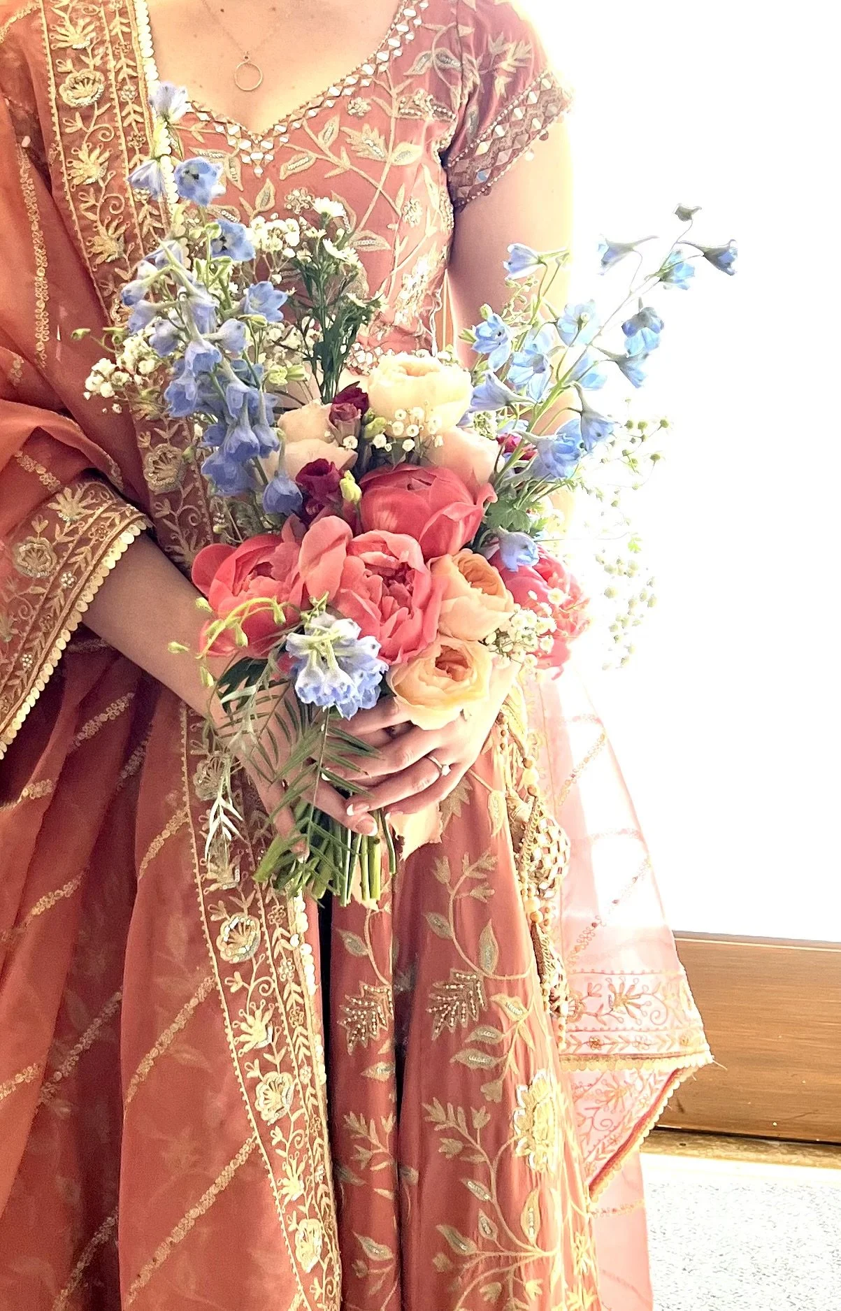 Bridal bouquet being held by bride at a Portland wedding wearing traditional gown, designed with peach and burgundy spring blooms and blue accents