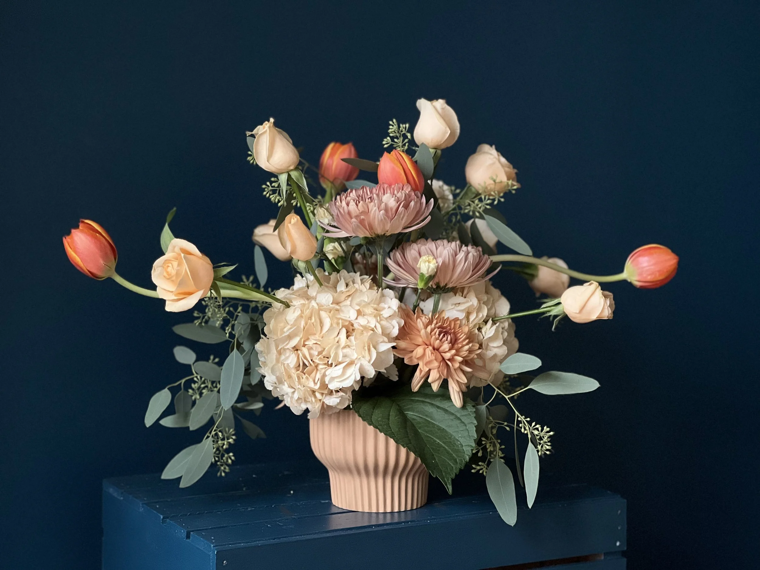 Neutral palette arrangement in low vase with mum base and sprawling peach roses and orange tulips