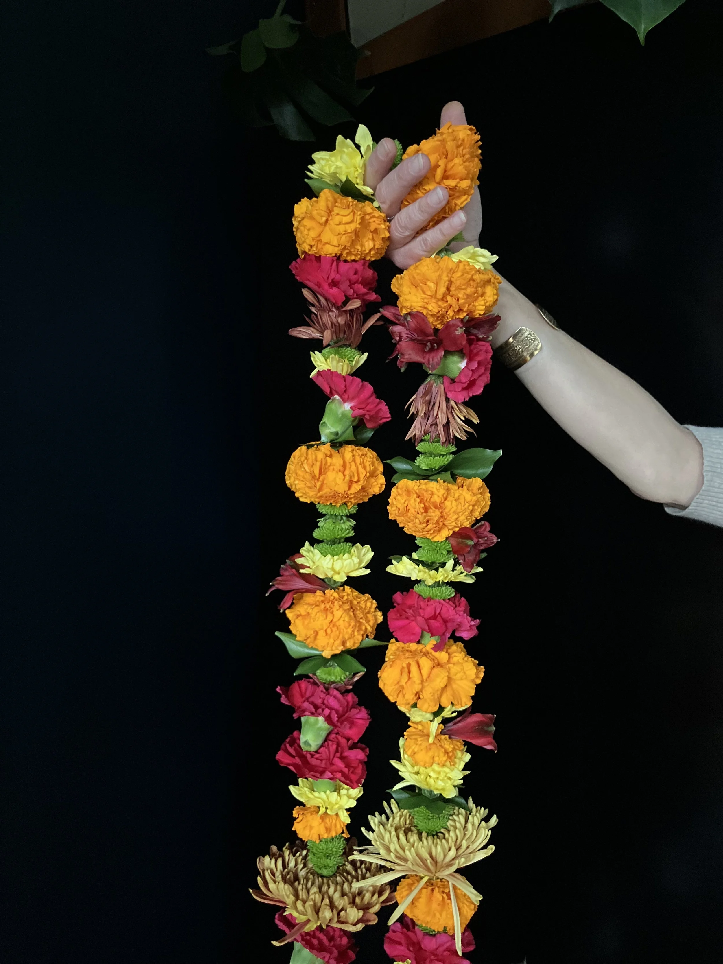 A beautiful and colorful handmade lei with orange marigolds, red carnations and yellow mums