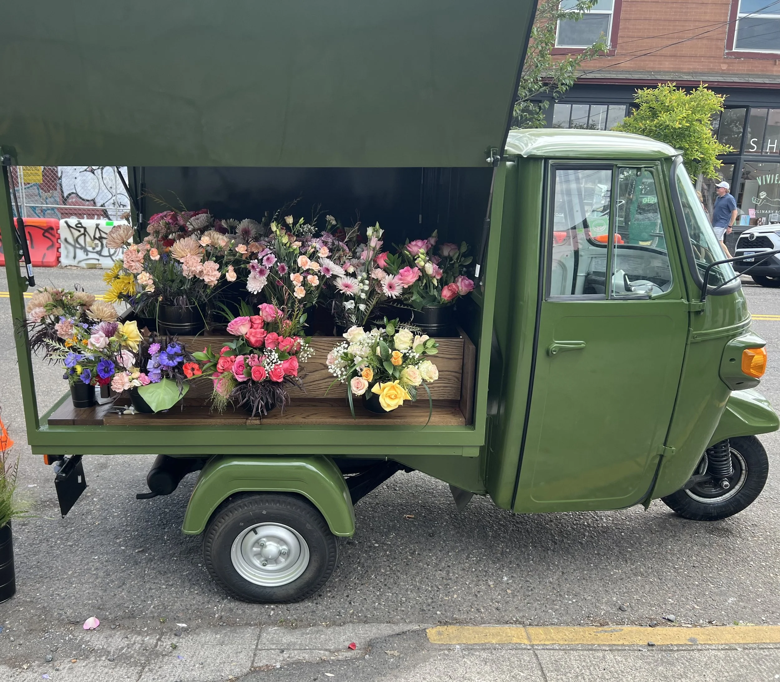 A small, hybrid truck with doors displaying bouquets and colorful flower stems on a street
