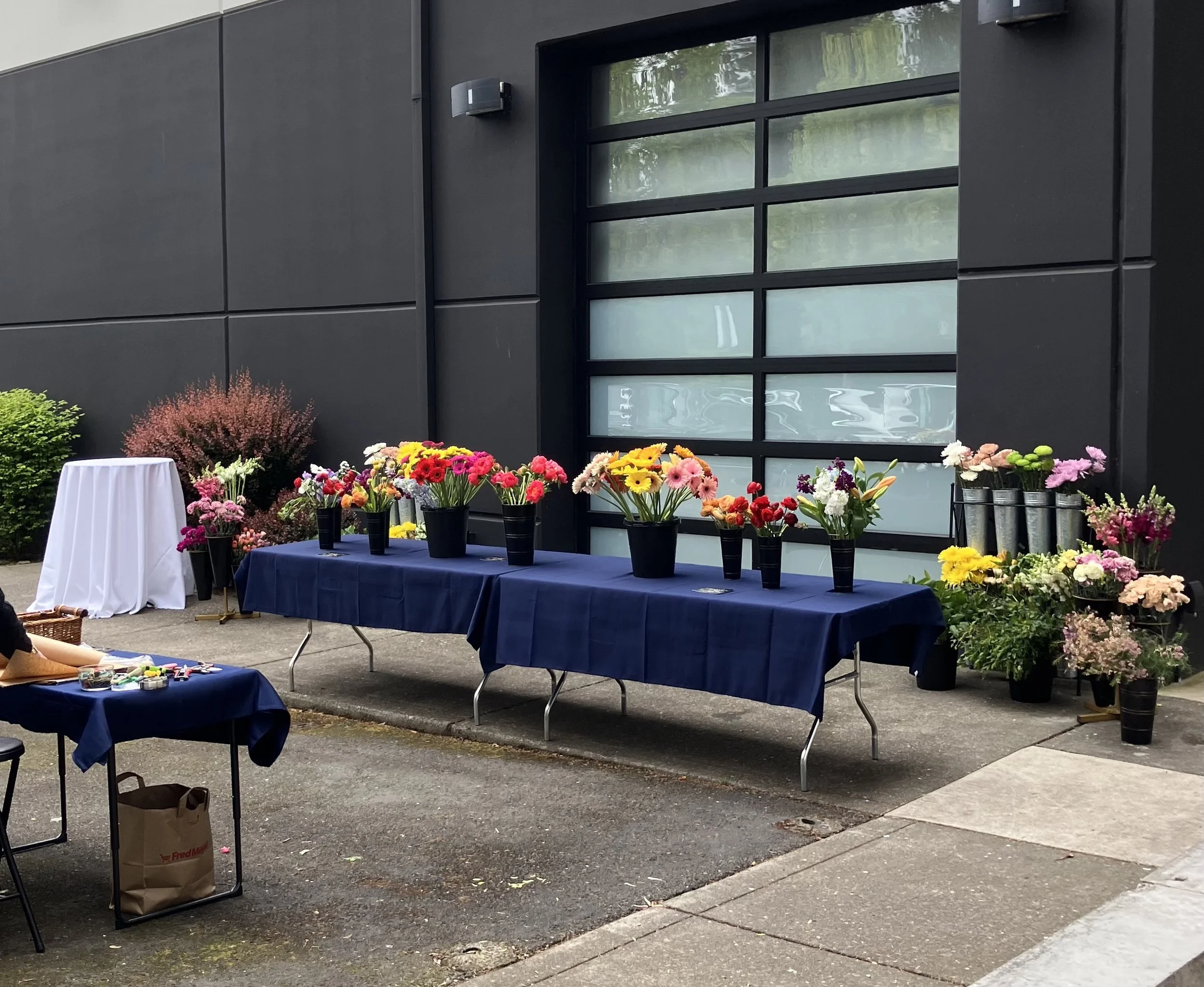 A DIY bouquet bar in Portland, with buckets of flowers set up on tables outdoors at a business event
