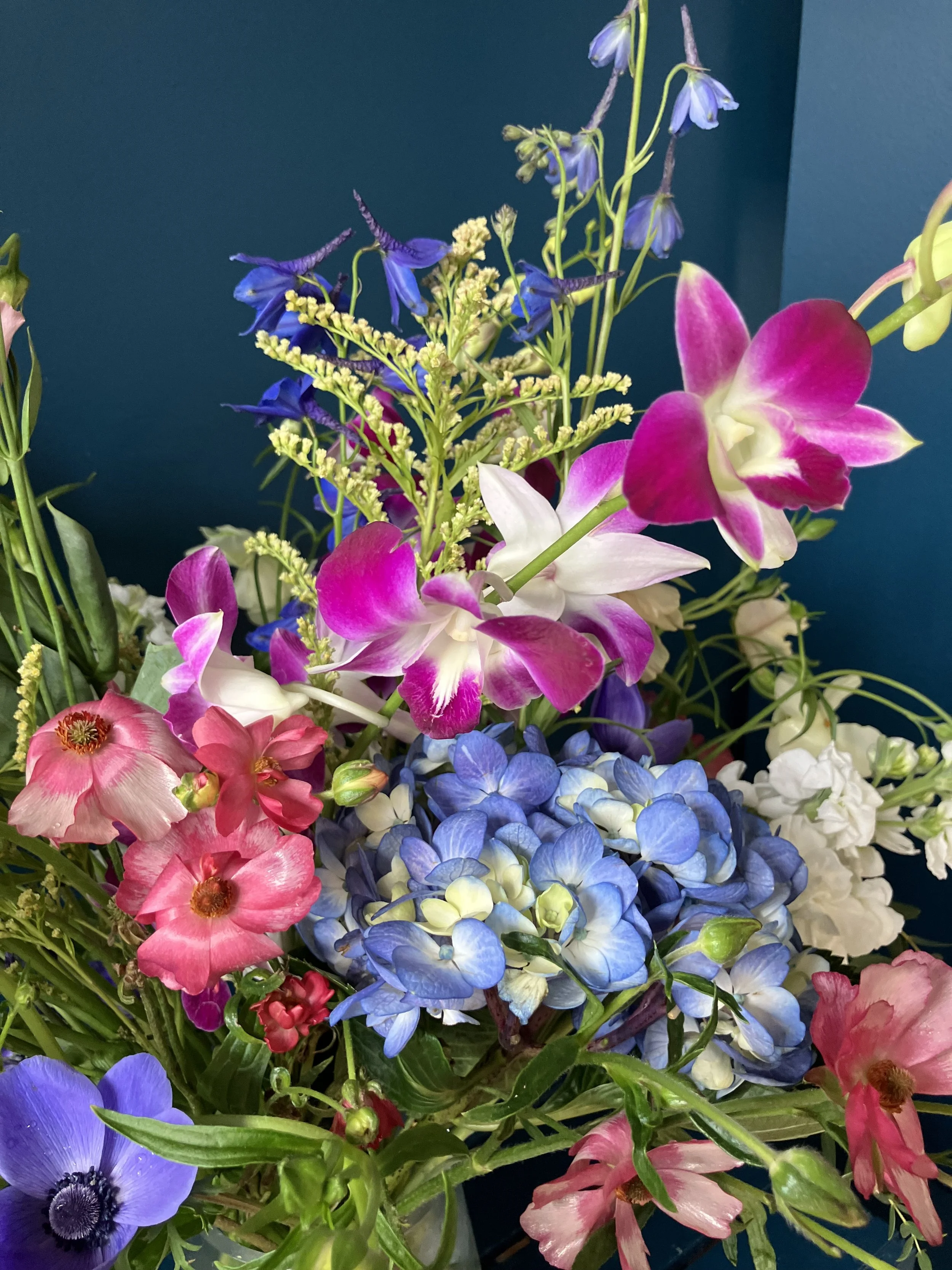 Close-up of butterfly ranunculus, purple anemone, and orchid in a sculptural garden-style spring arrangement with soft pastel tones