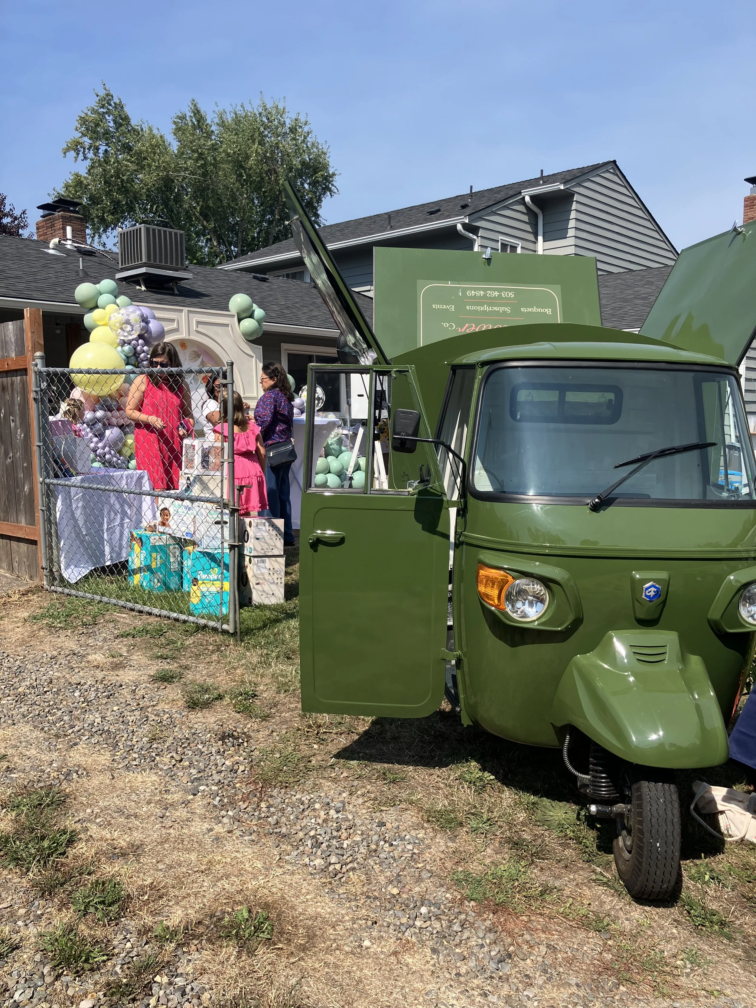 Scene at an outdoor baby shower in Portland, with balloon, gifts, guests, and a green truck with a bouquet bar