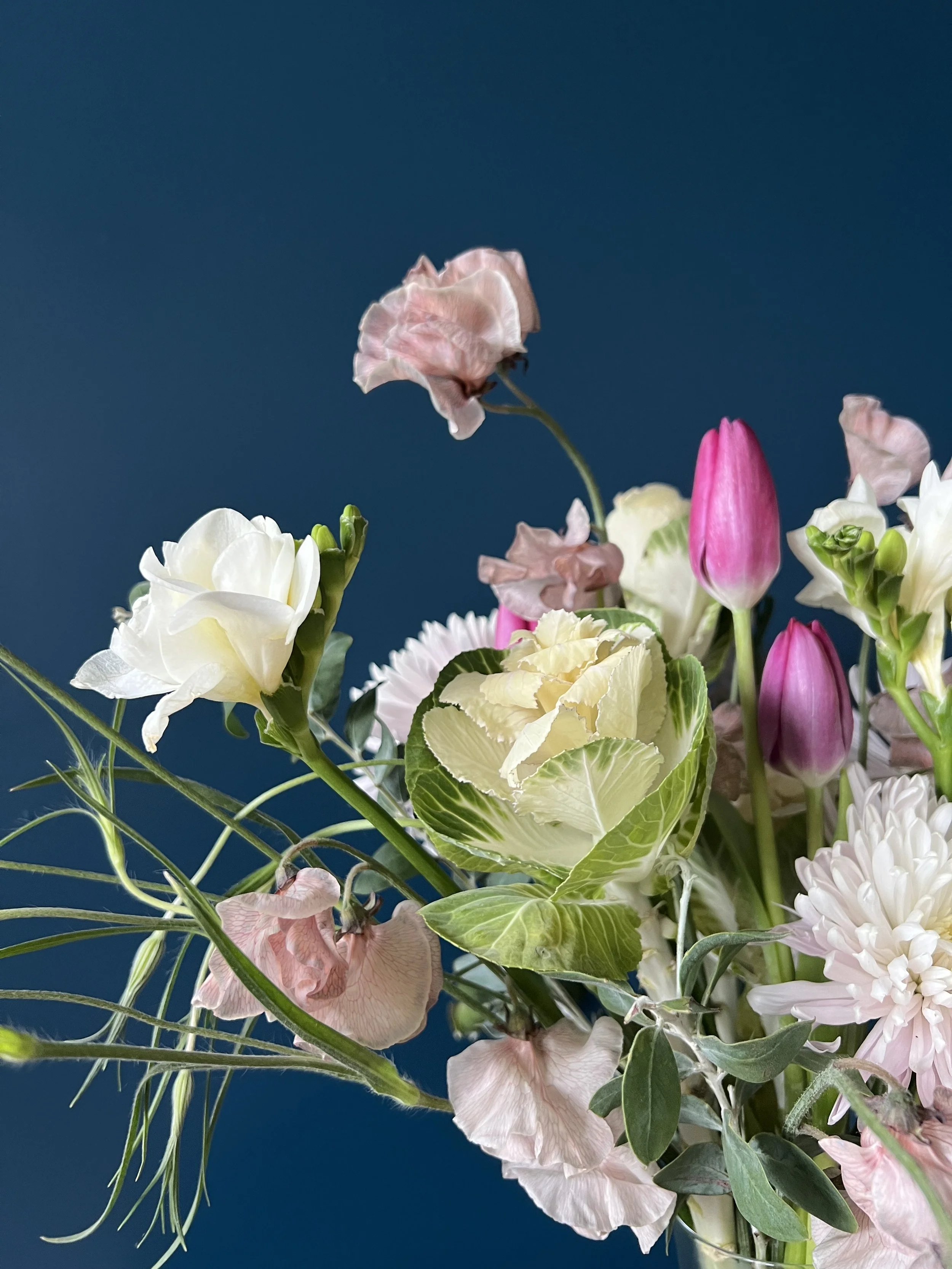 Made to express sympathy in flowers, this close up highlights white freesia, pink sweet pea, and purple tulip over a chrysanthemum