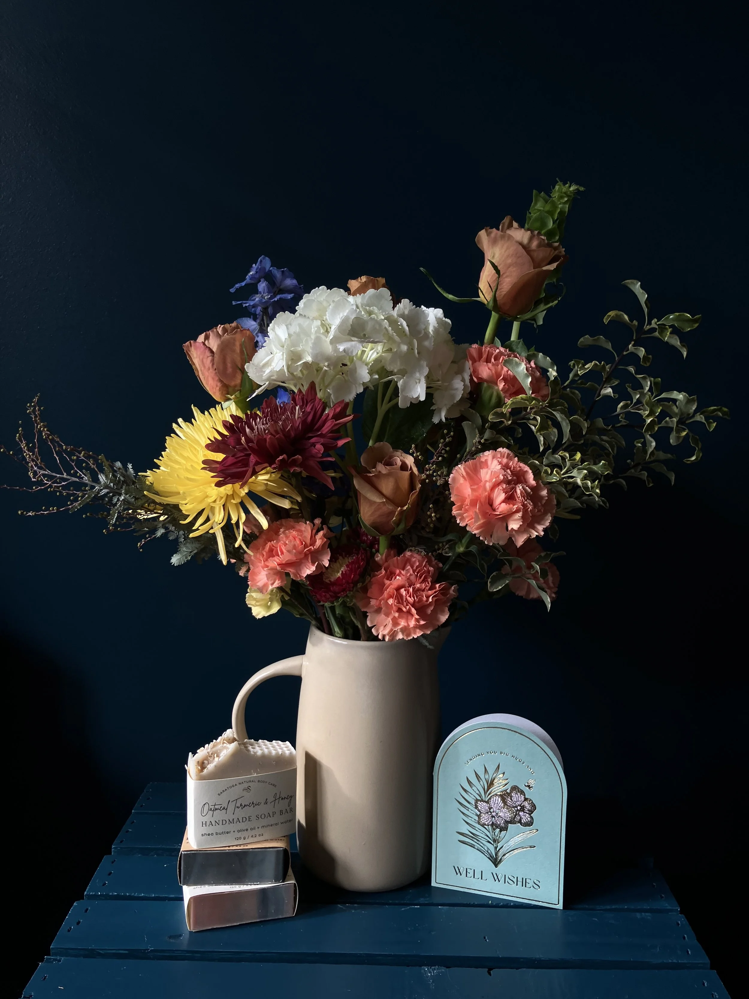A more blush colored version of this arrangement in a pitcher with carnations, dahlias, and roses against a dark background