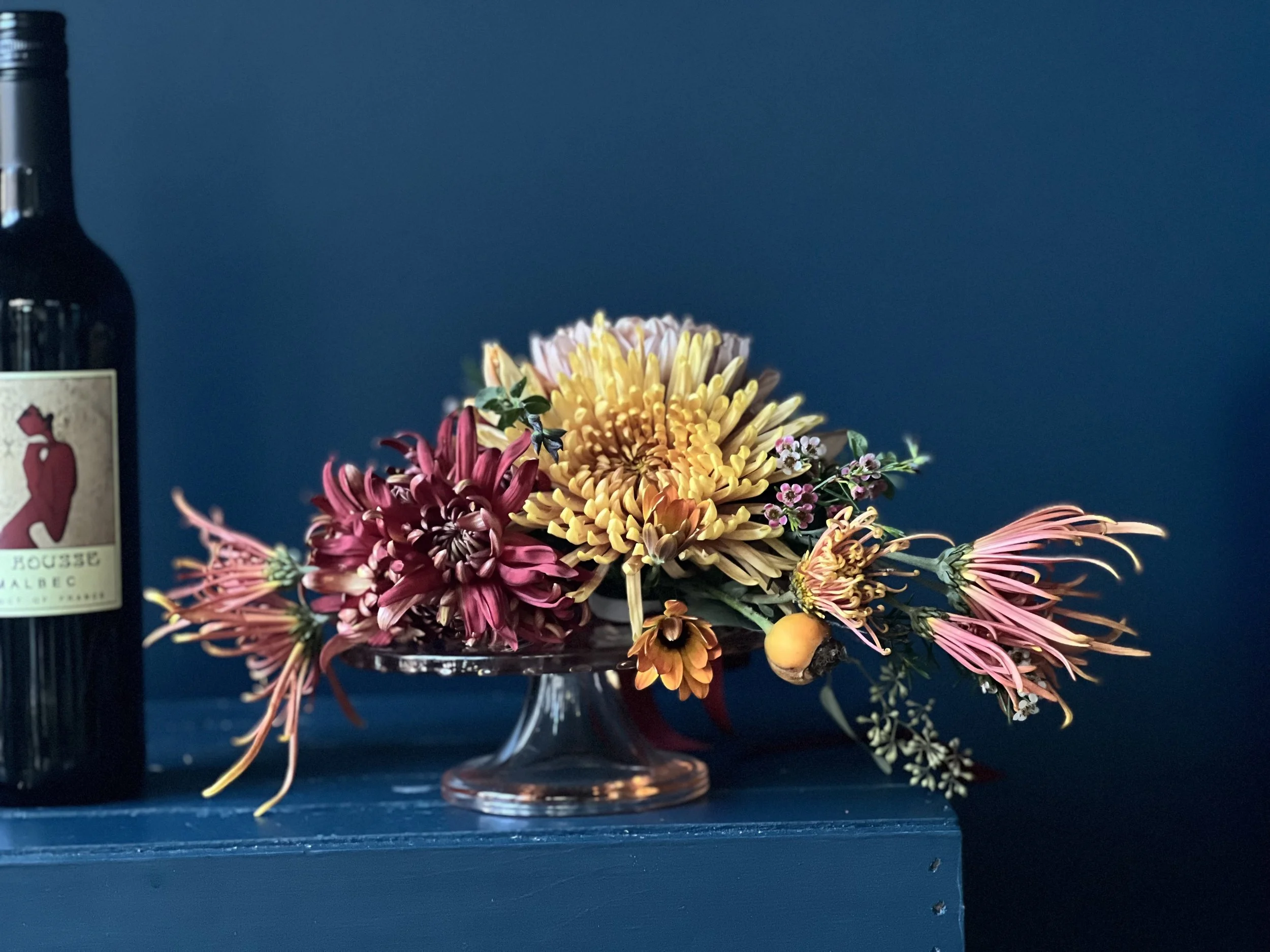 Bottle bouquet in fall with mums taken off the wine and on its side used as a side floral piece
