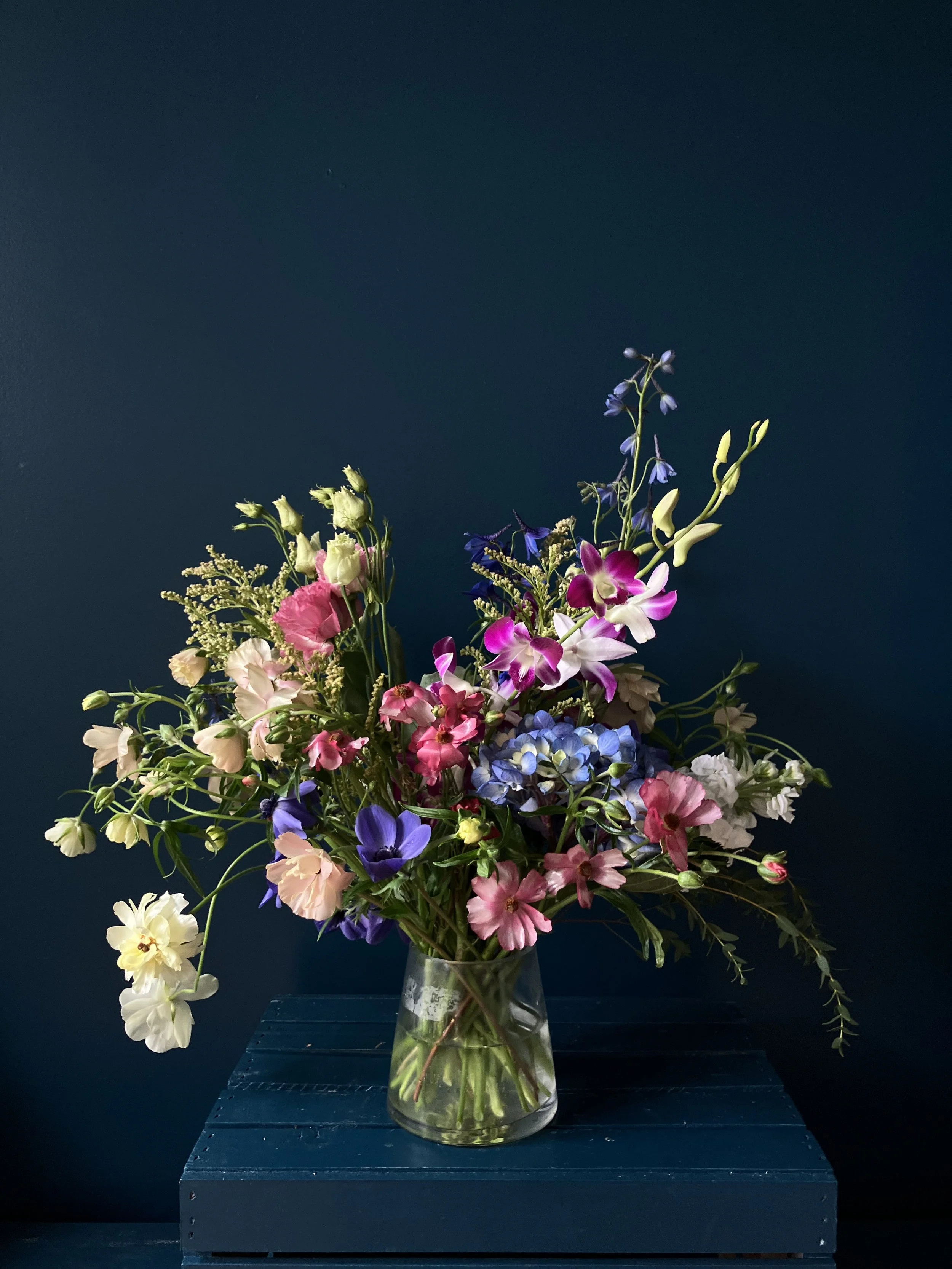 Large airy spring flower arrangement in low glass vase with ranunculus, anemone, hydrangea, and orchid for Mother’s Day delivery in Portland
