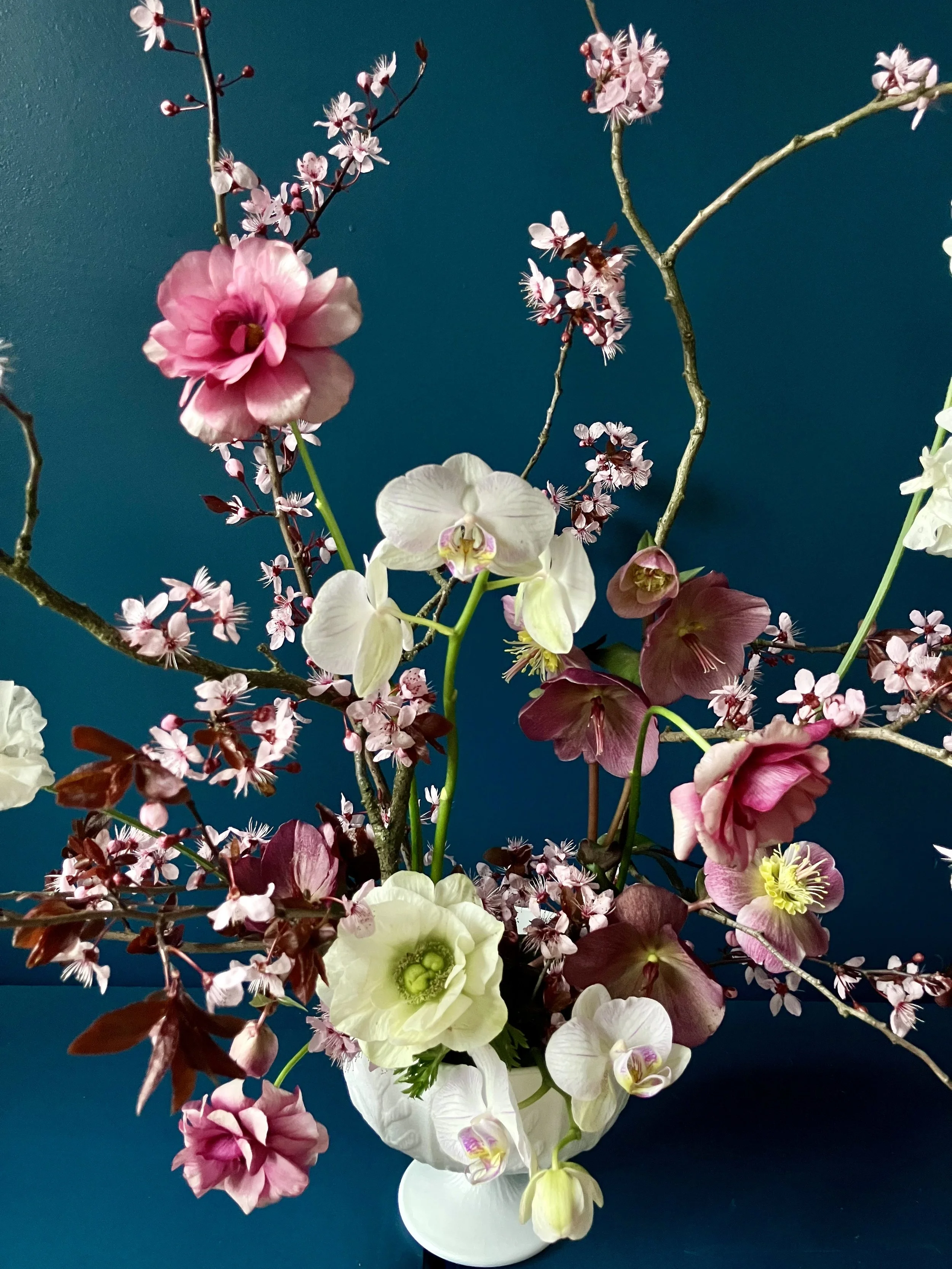 Pink butterfly ranunculus and reddish and white hellebore in a seasonal floral design with cherry blossom branches