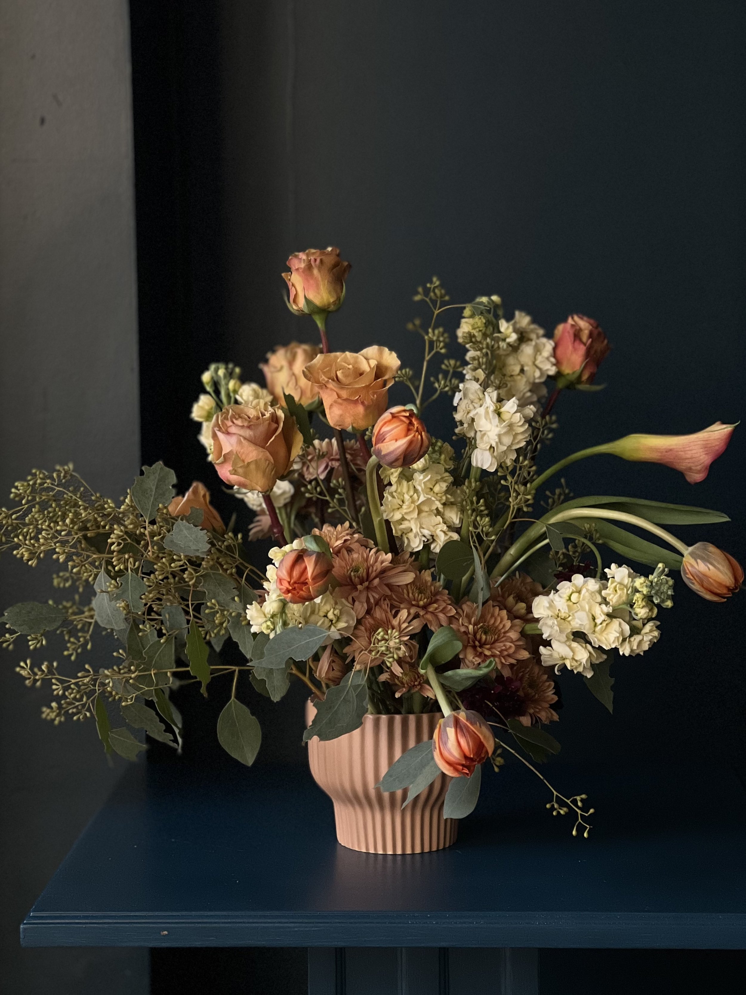 Blush colored roses, calla lilies and tulips with white stock and eucalyptus arranged in a ceramic vase