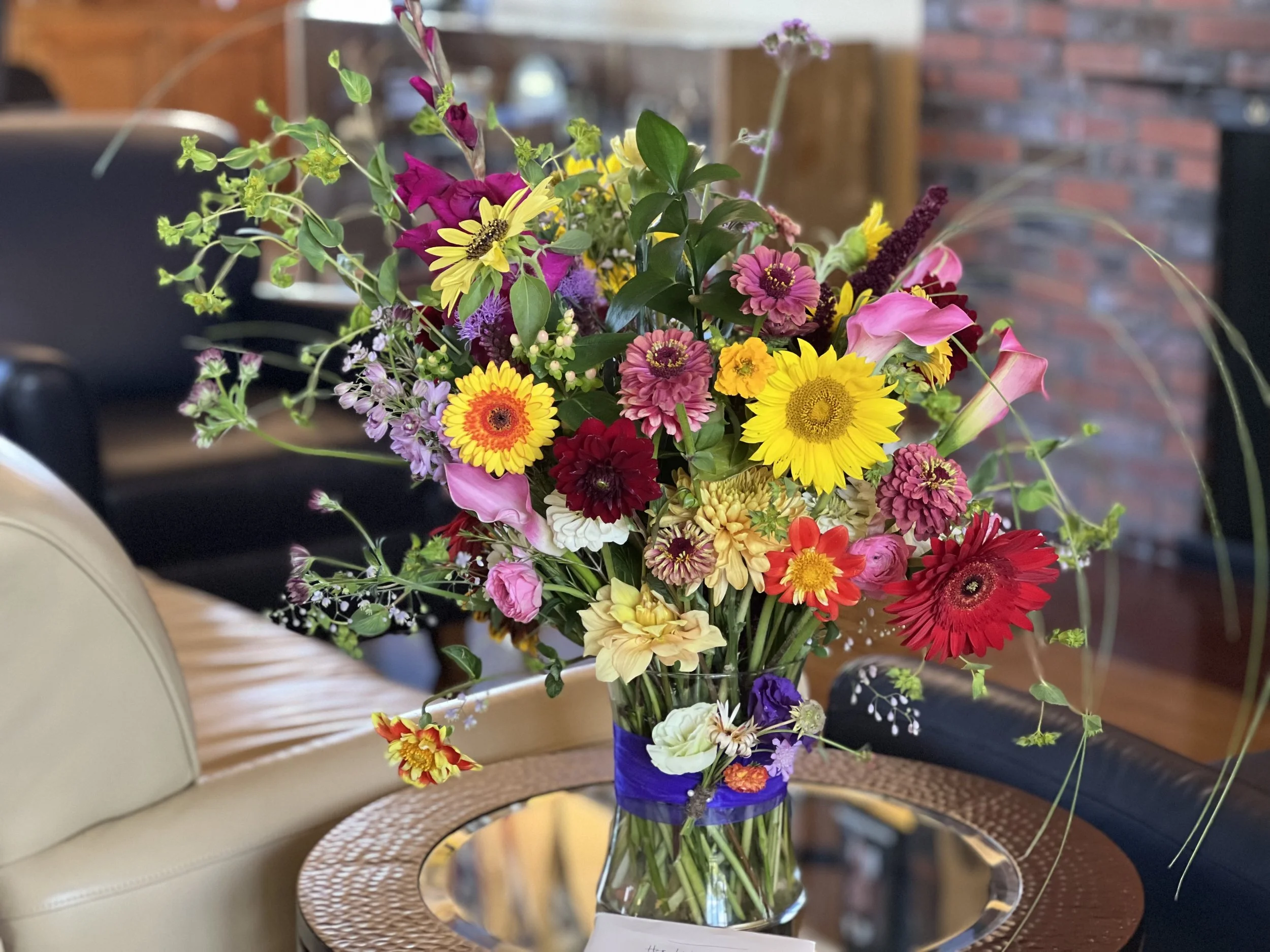 A colorful sympathy arrangement in Portland in a reception room, made for a summer life celebration using zinnias, daisies, sunflowers, and calla lilies