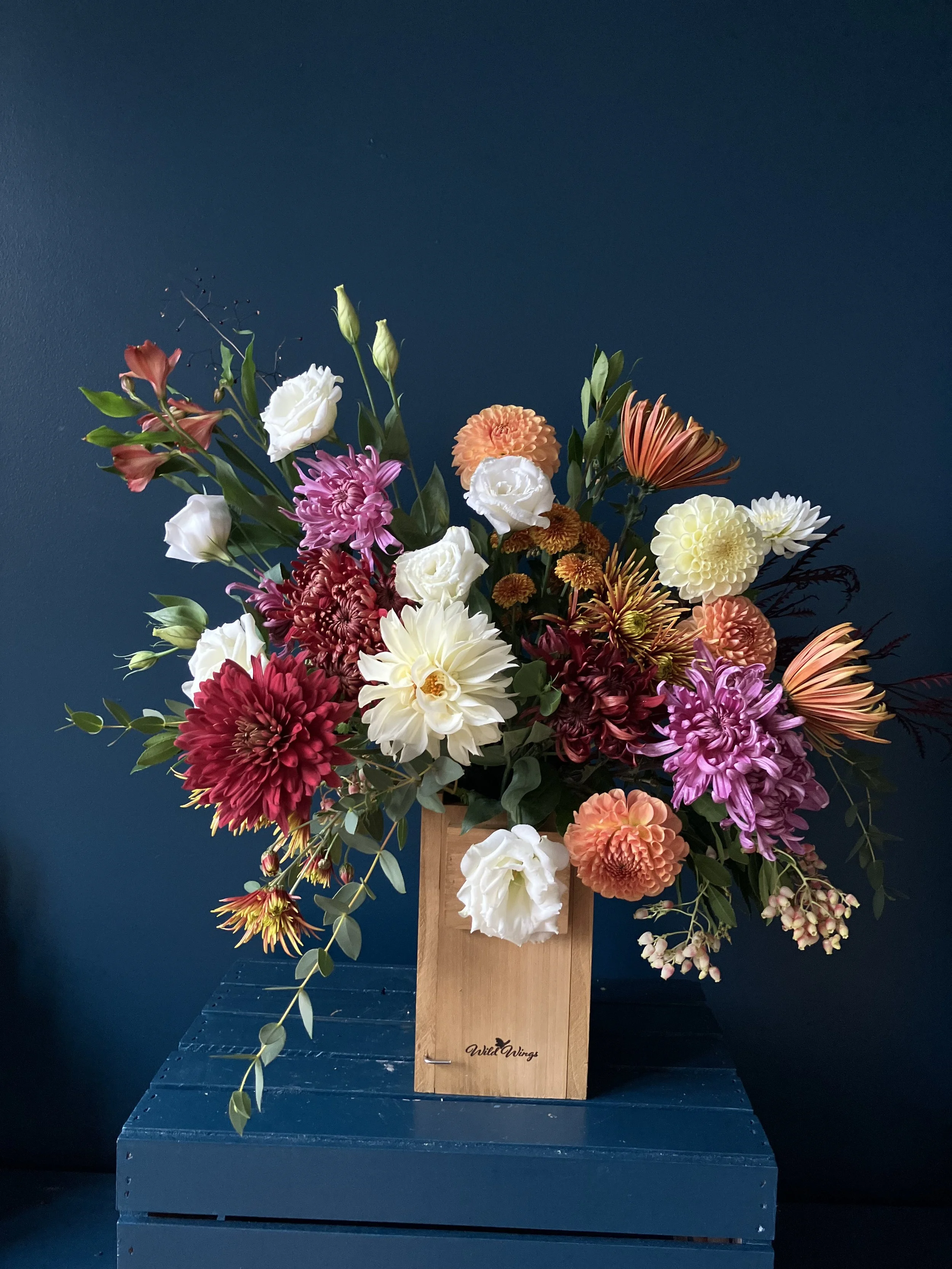 Designed in Portland, OR, a red and orange colored seasonal arrangement of heirloom mums, dahlias, lisianthus