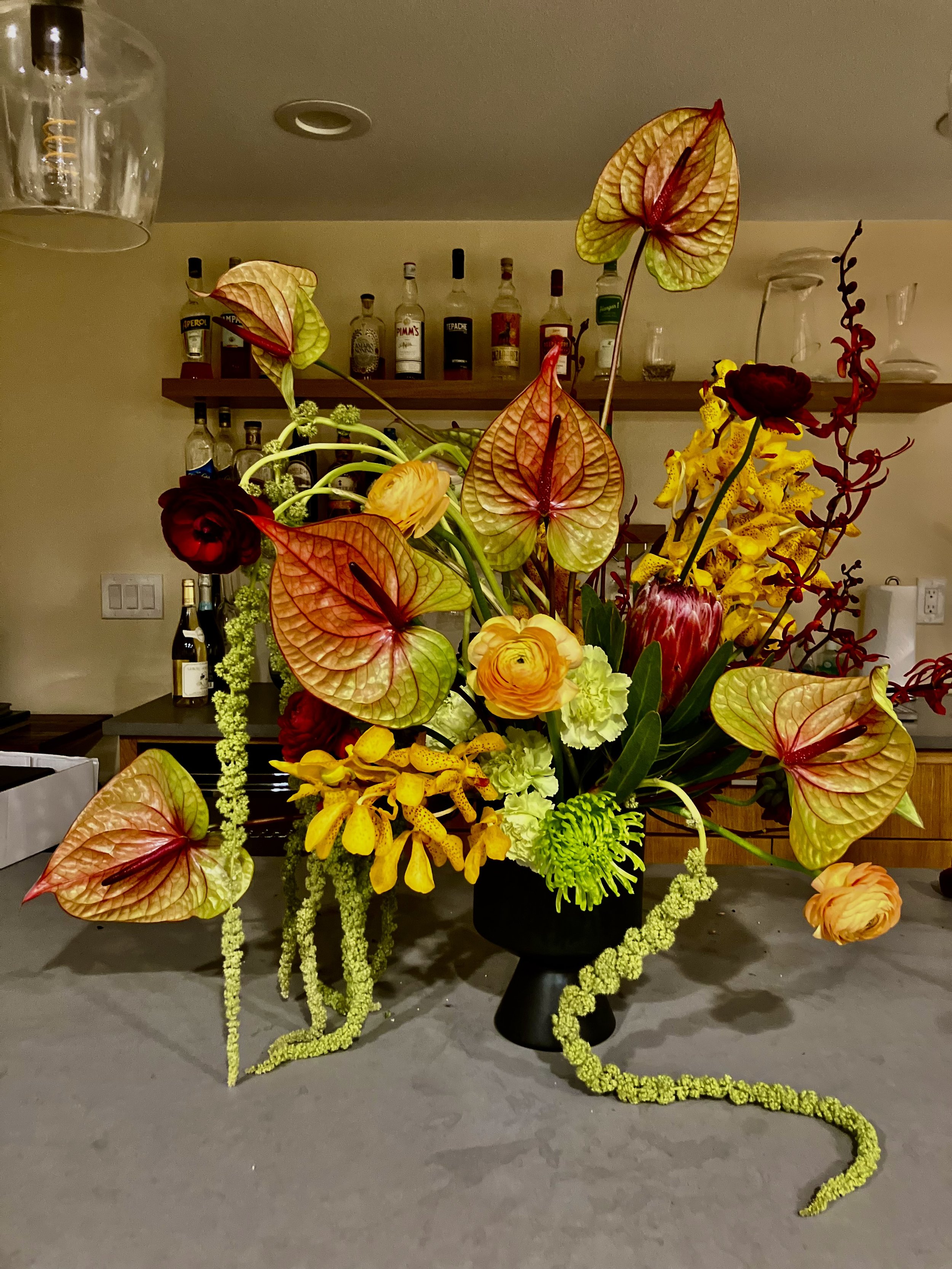 To celebrate a Portland wedding event at home, this luxury arrangement features tropicals like anthurium, orchids, and protea with ranunculus in yellows, reds, greens