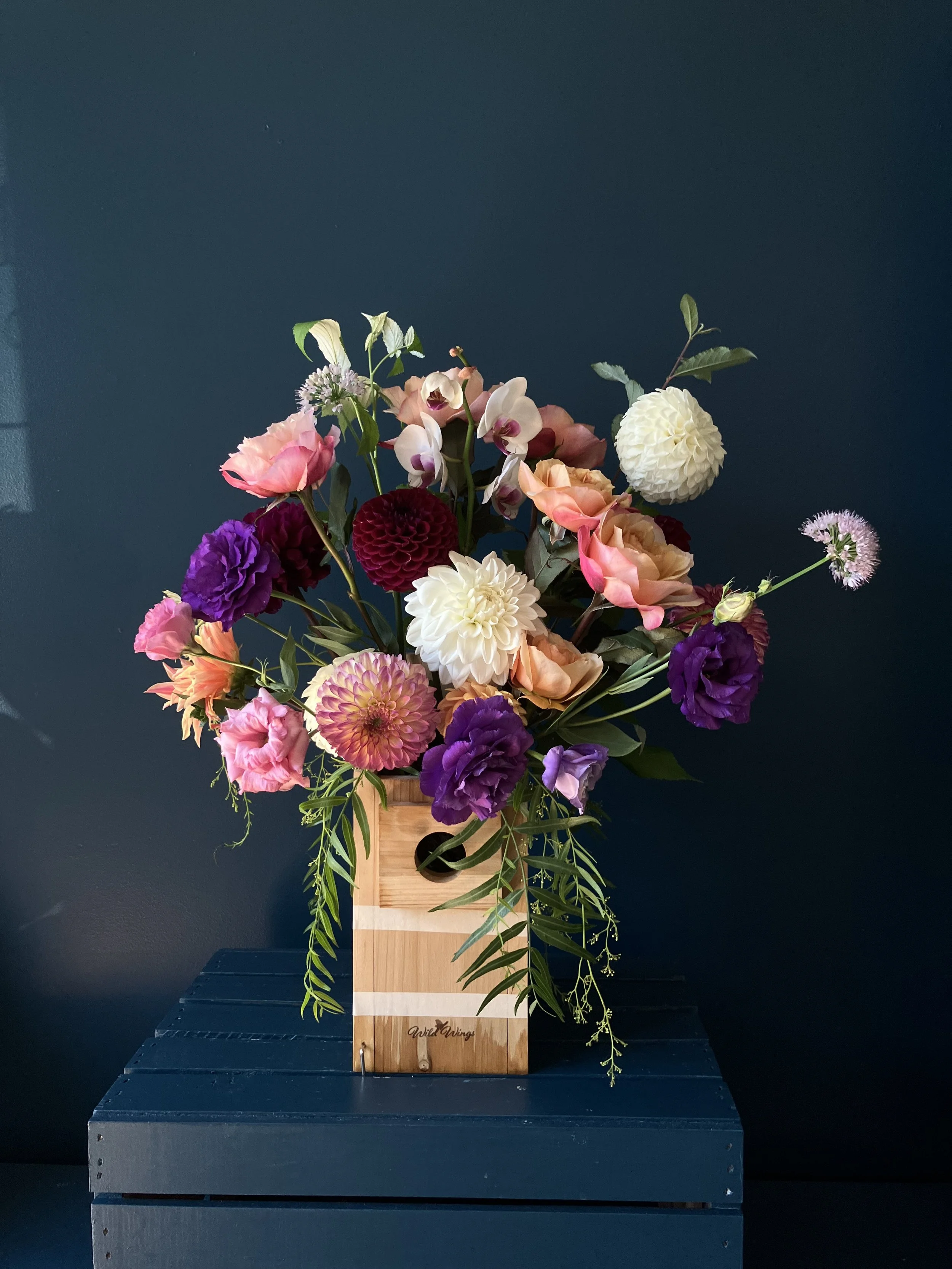 Here is a summer arrangement in a unique vessel full of flowers like roses and dahlias