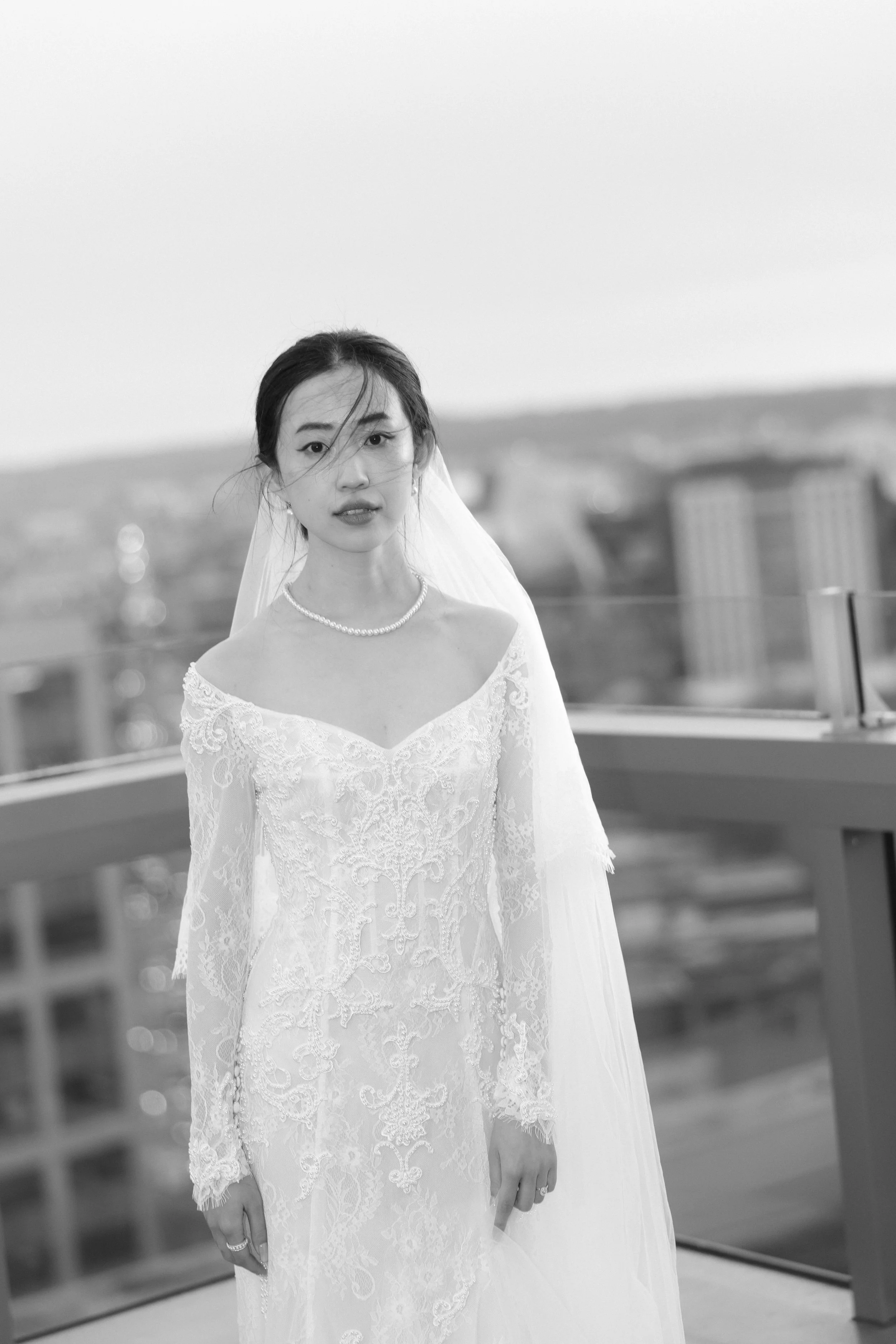 Black and white photo of a woman in a wedding dress and veil standing on a rooftop.