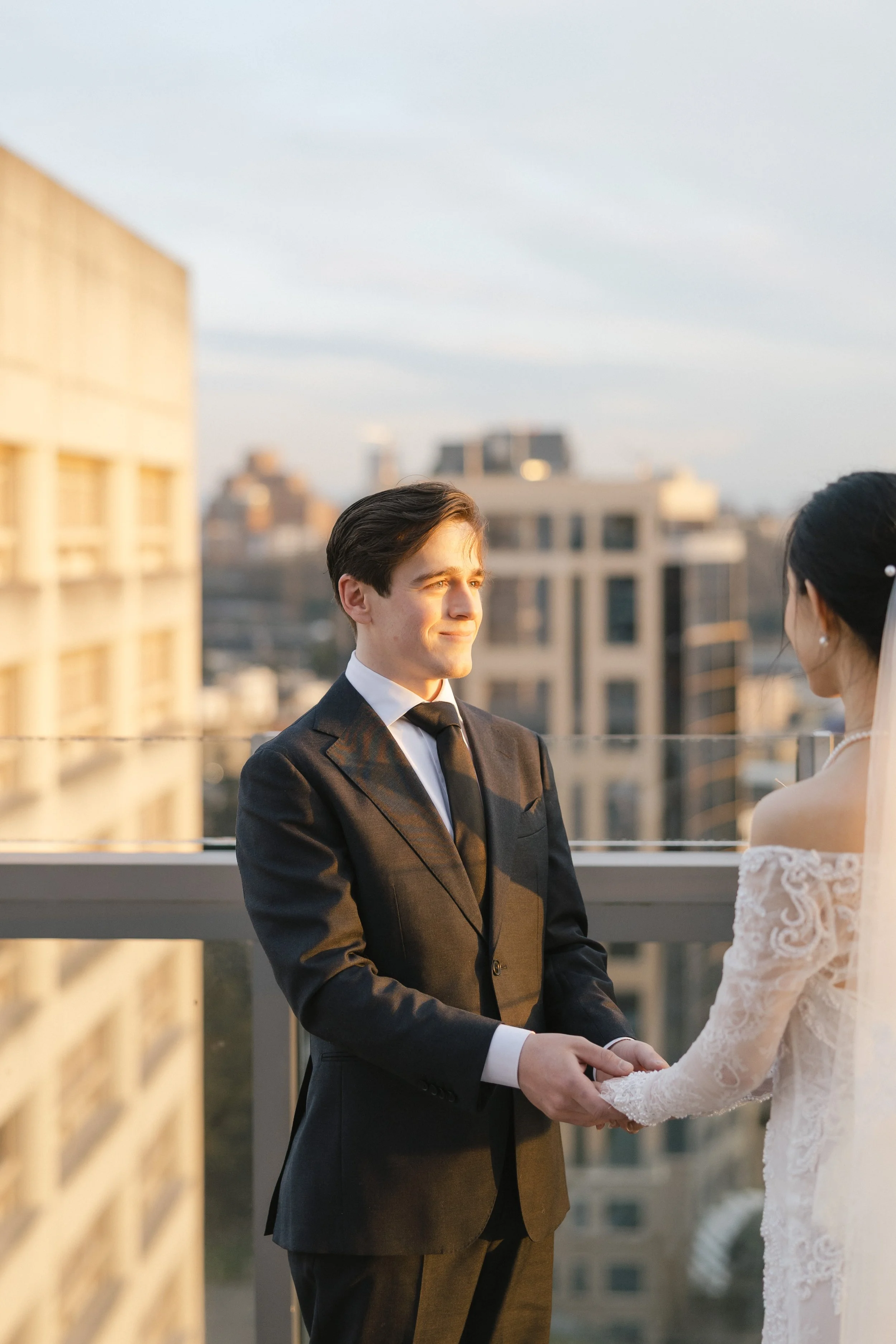 A bride and groom holding hands during their wedding ceremony on a rooftop at sunset.