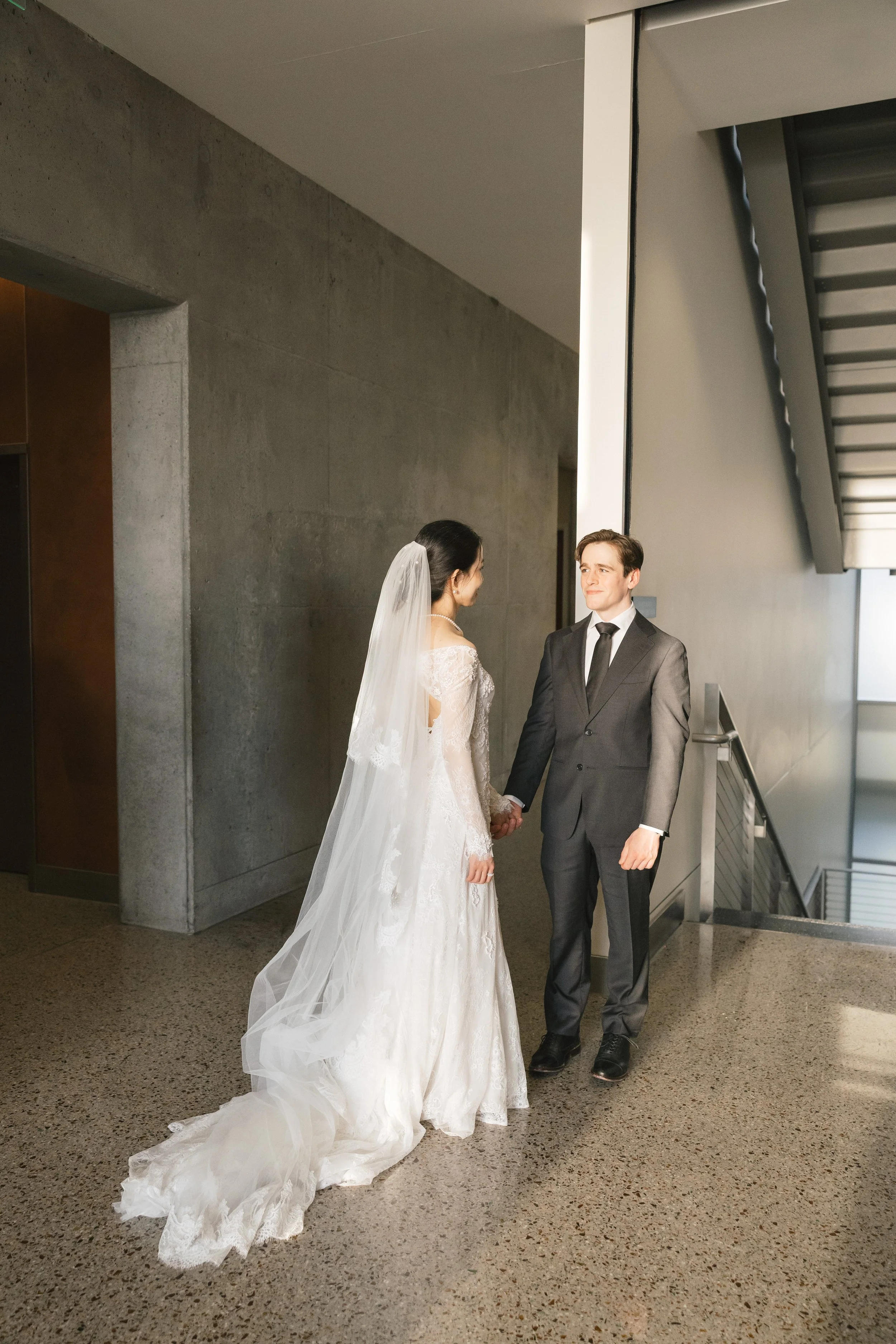 A bride and groom holding hands and facing each other in a modern, indoor setting.
