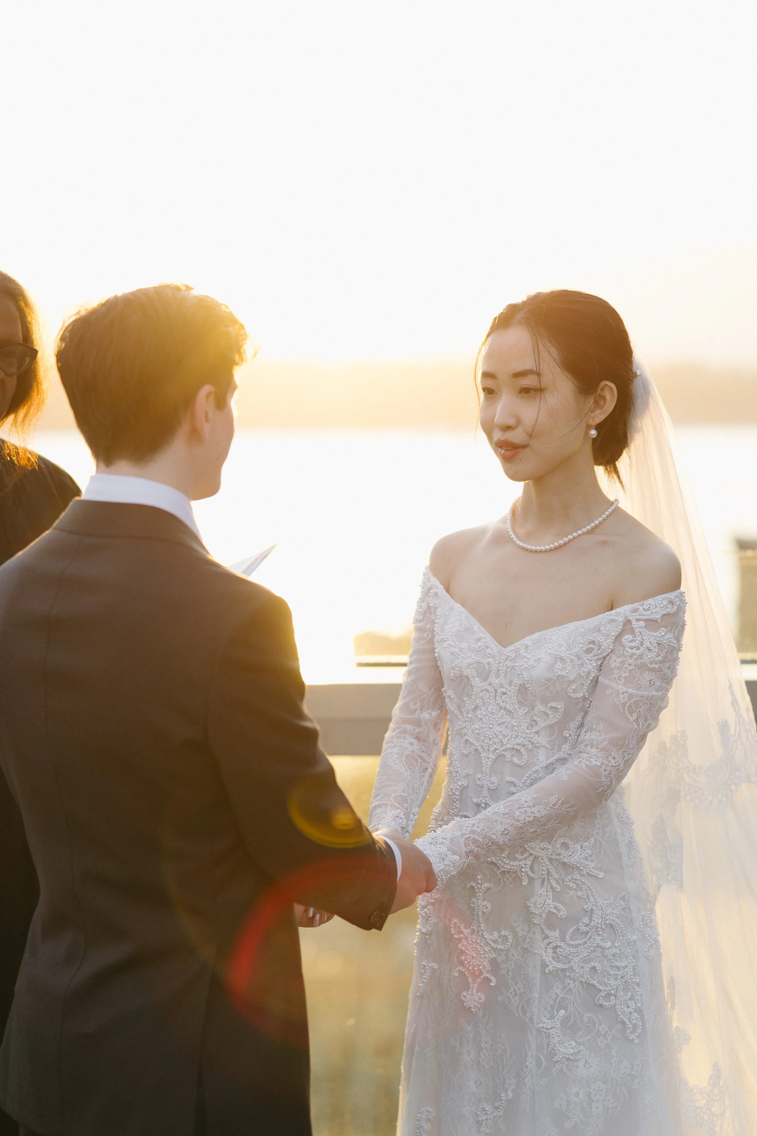A bride and groom holding hands during their wedding ceremony outdoors at sunset.