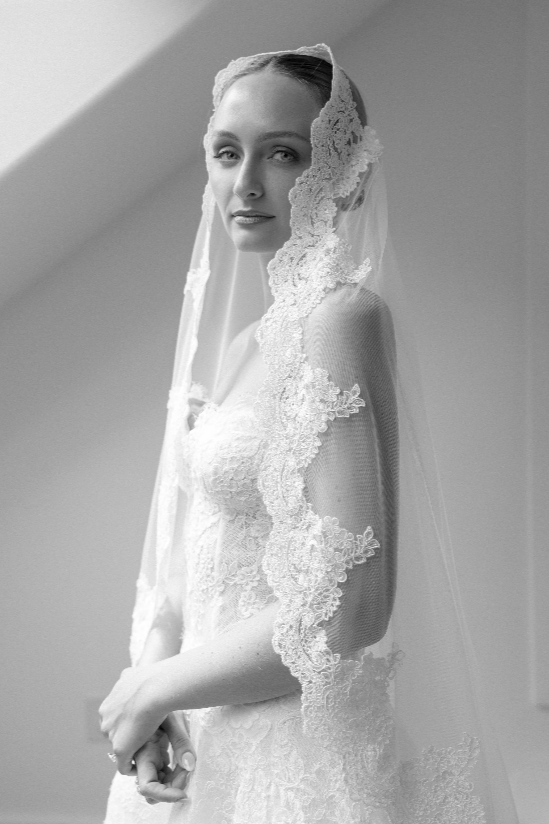 A woman in a wedding dress with a lace veil looking at the camera.