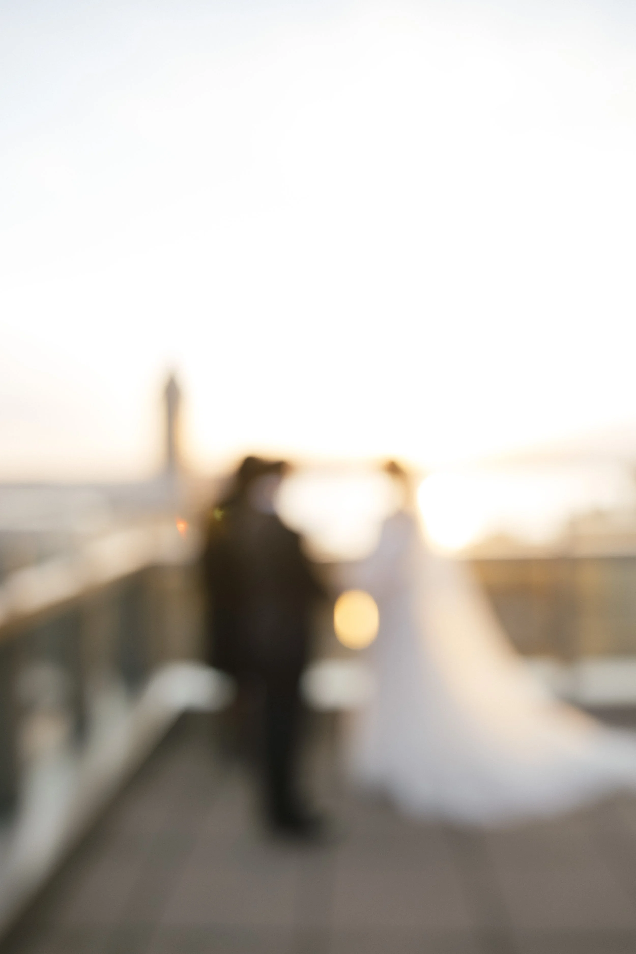 Blurred photo of a bride and groom on a bridge at sunset.