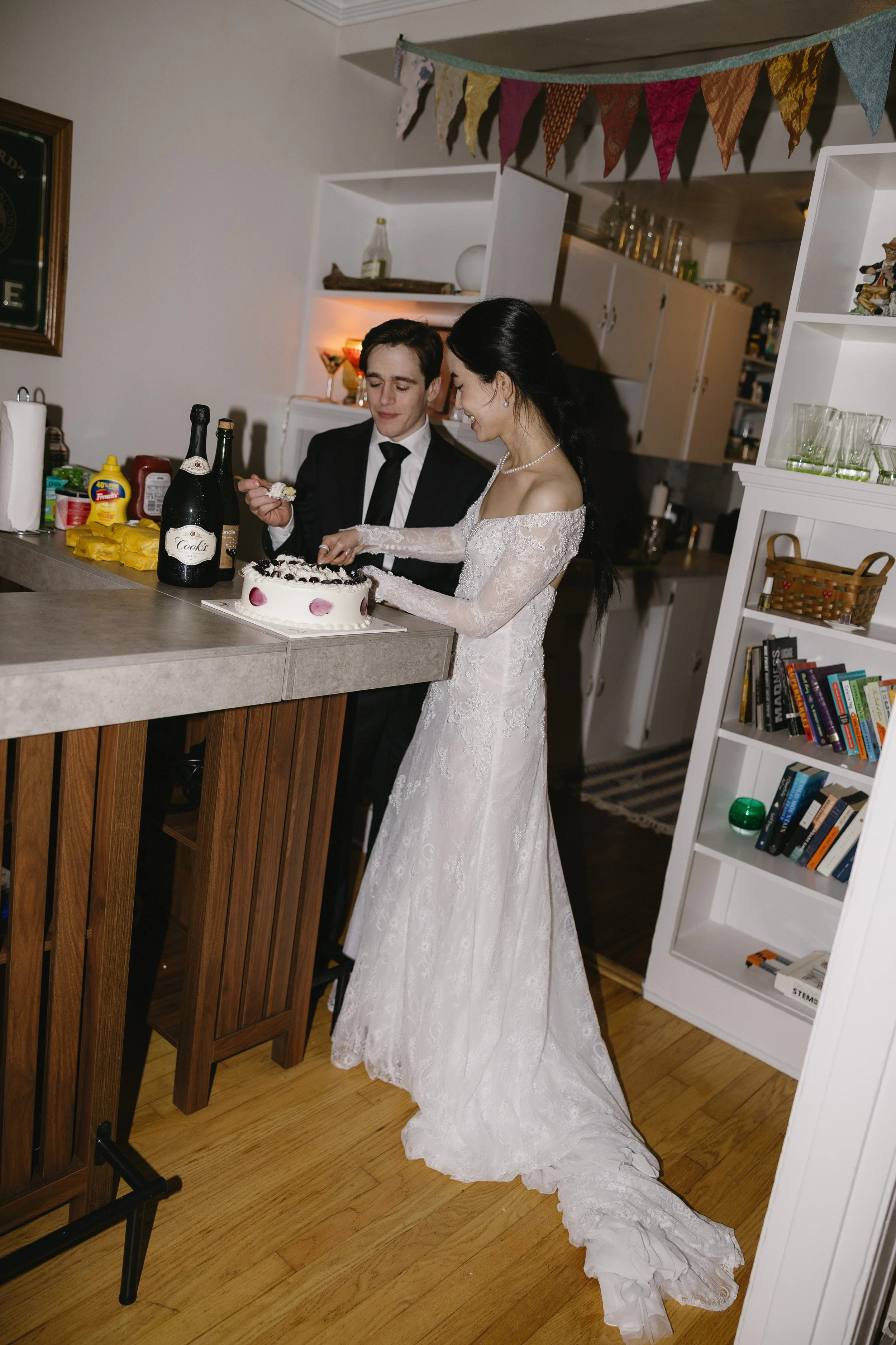 A bride and groom cutting a wedding cake together at a home celebration.
