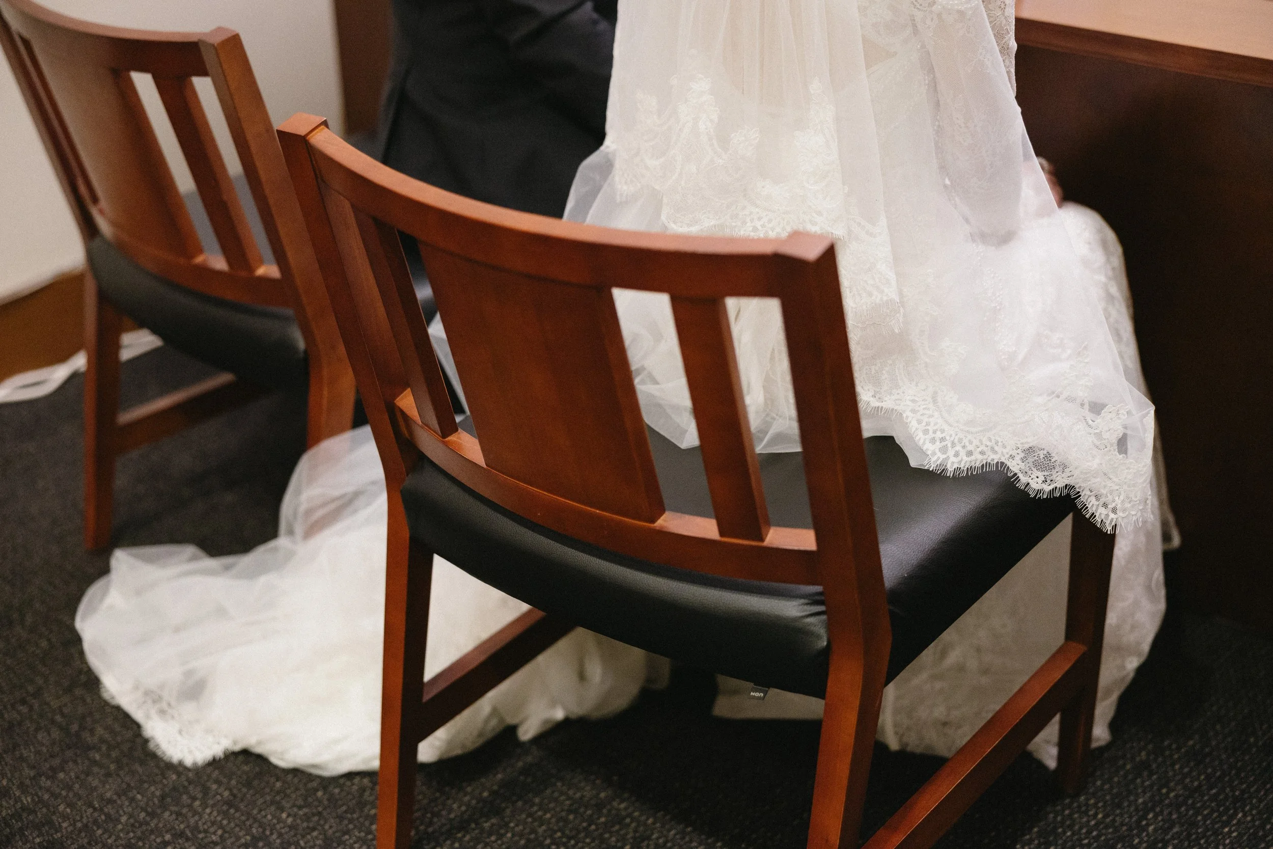 Clothing of a bride resting on a chair and near a pew at a wedding ceremony