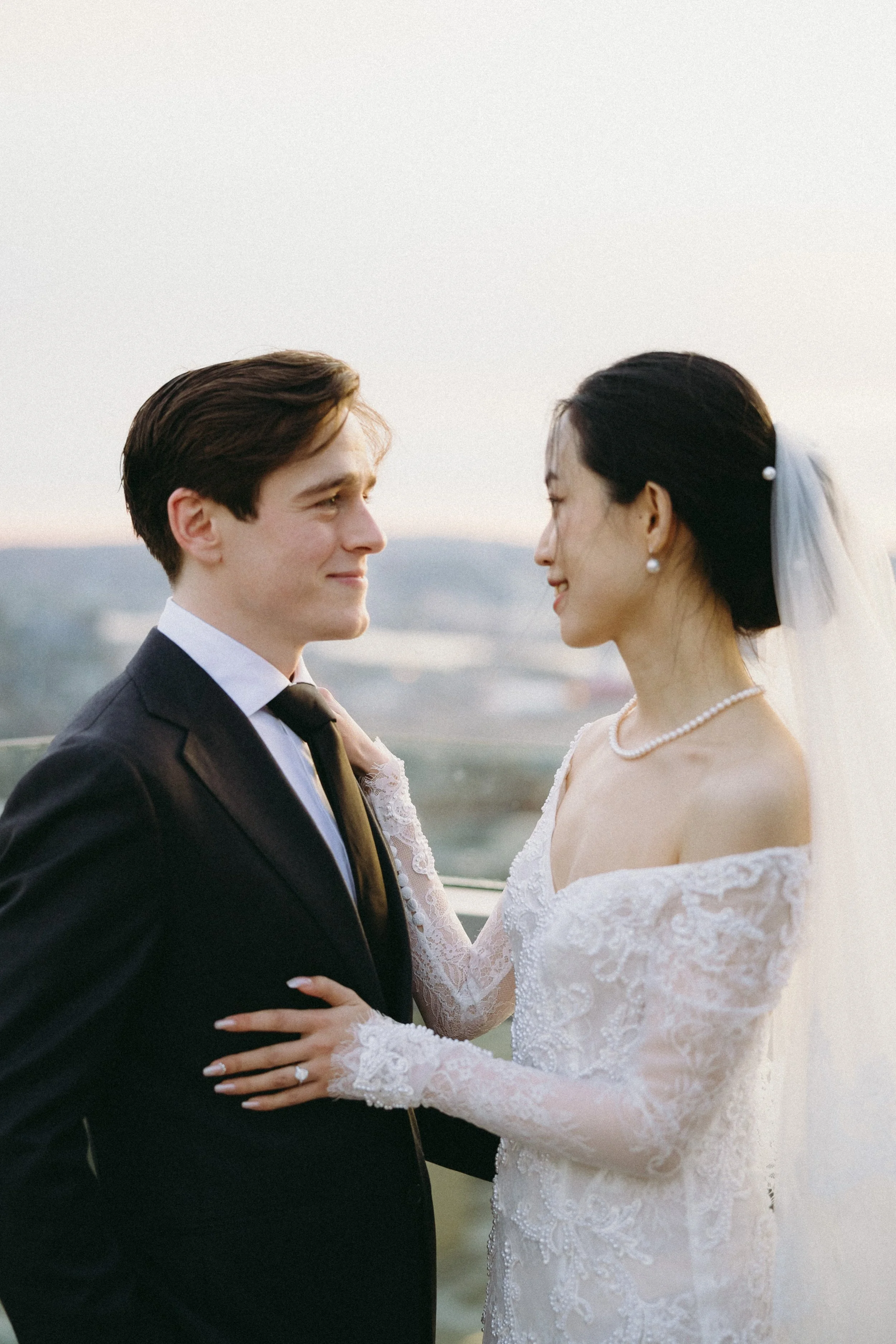 A bride and groom stand close together, gazing into each other's eyes outdoors during their wedding, with a scenic background.