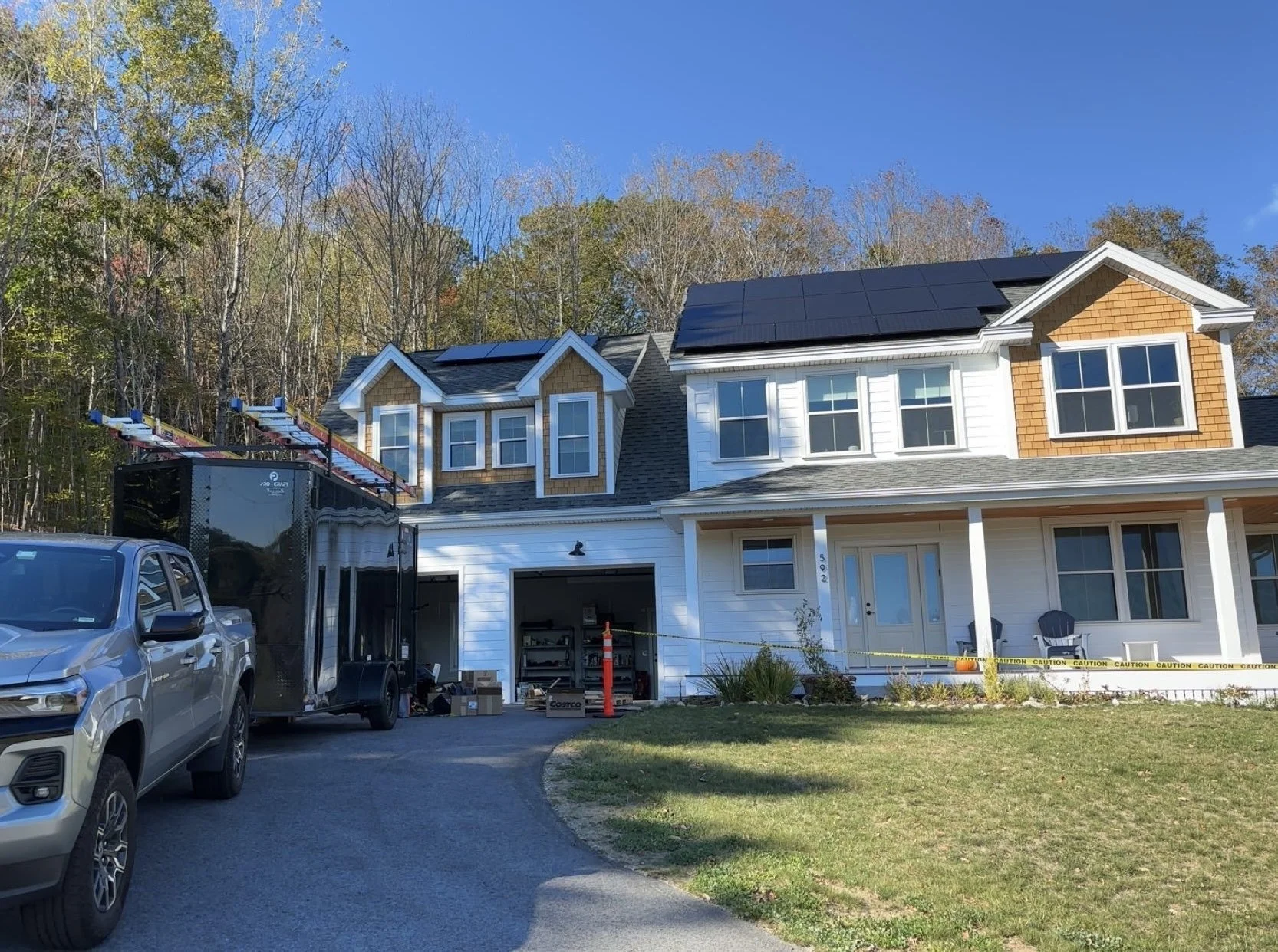A two-story house with solar panels on the roof, a driveway, and a garage. Construction equipment and materials are present, with caution tape around the porch area.