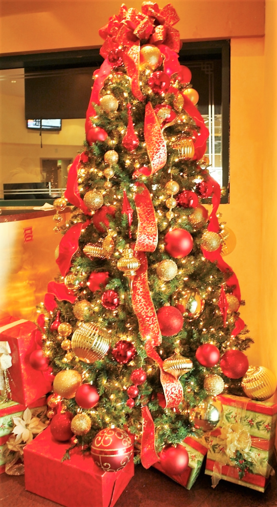 A decorated Christmas tree with red and gold ornaments, ribbons, string lights, and presents underneath.