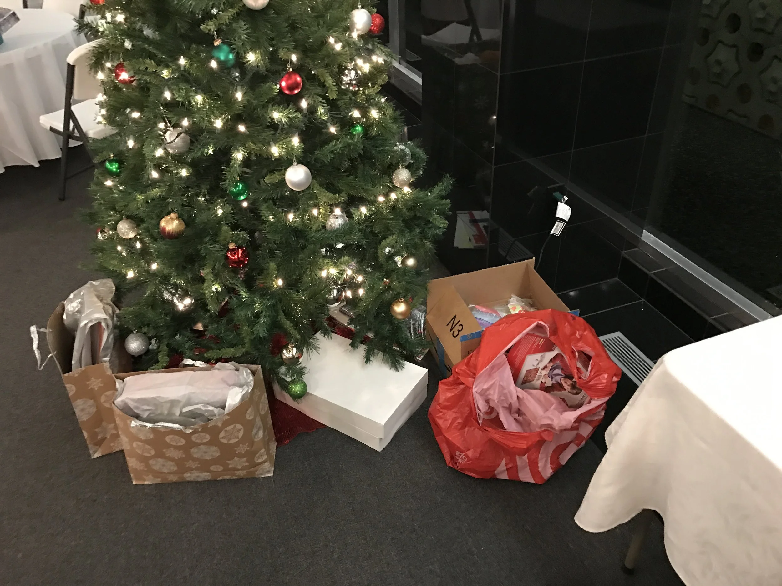 Christmas tree with ornaments and lights next to wrapped and unwrapped gift bags and boxes on the floor.